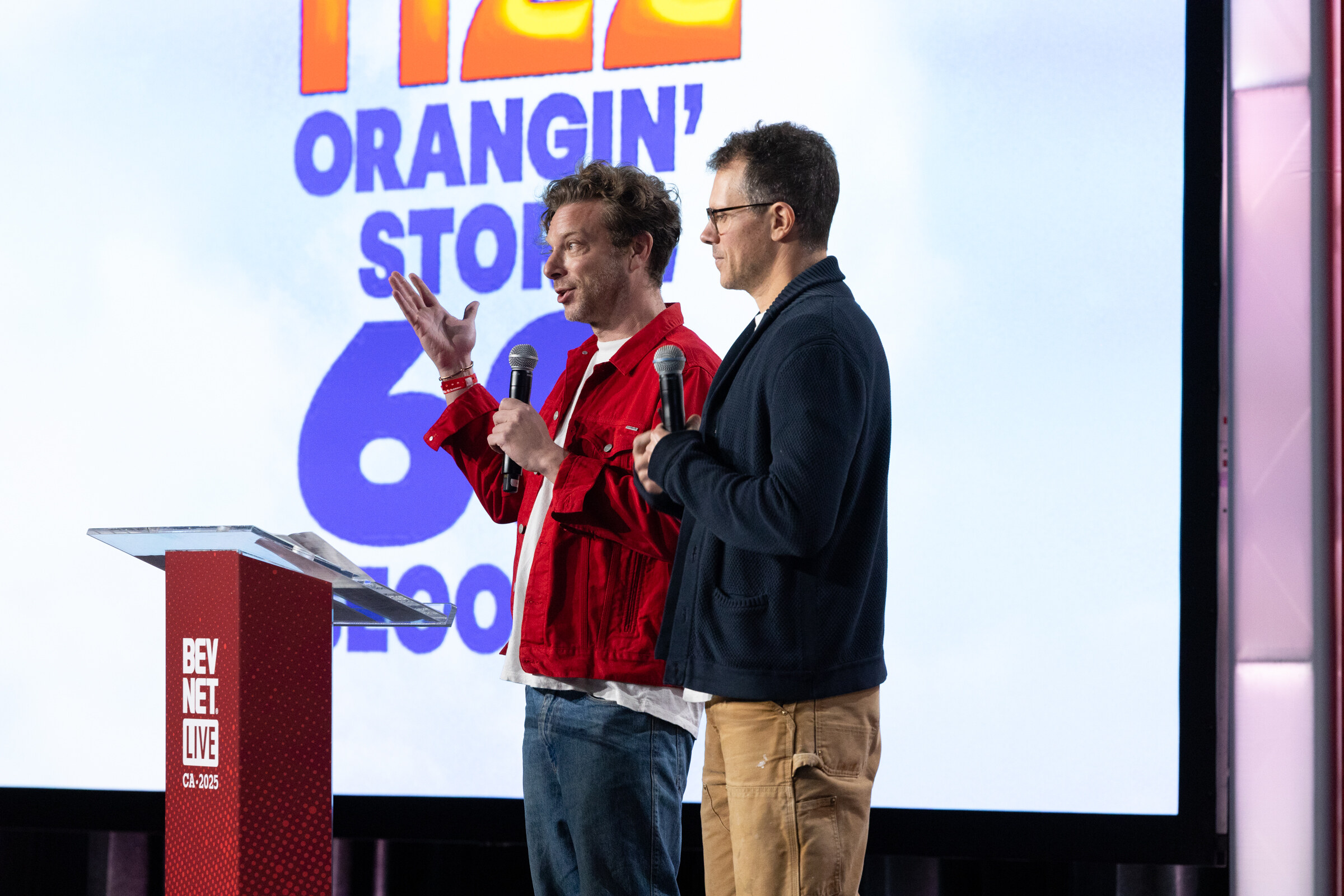 Two men, one in a red jacket, present in front of an orange slide.