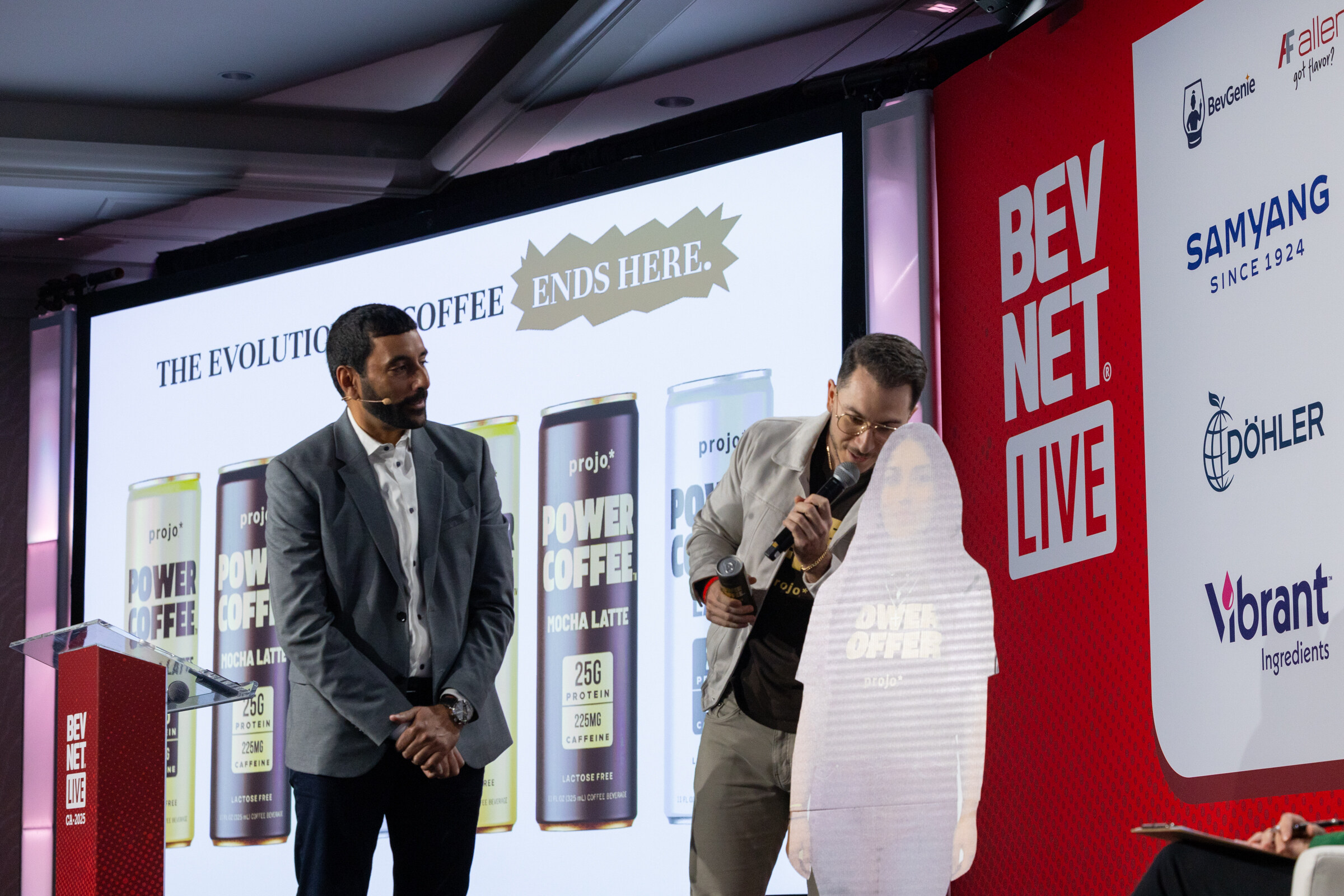 Two men stand on stage in front of a Power Coffee slide.
