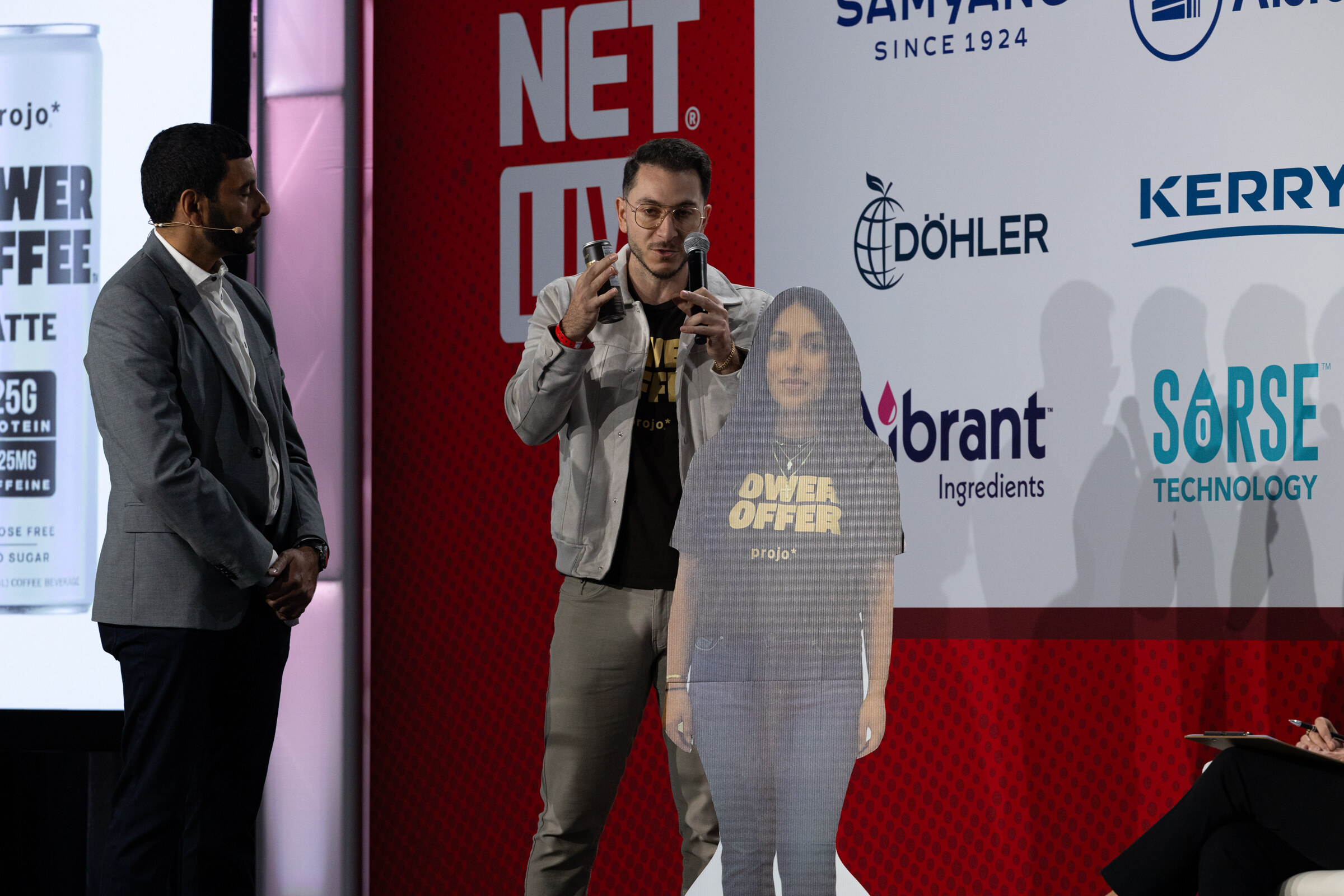 A man speaks beside a standing cutout in a Power Coffee shirt.