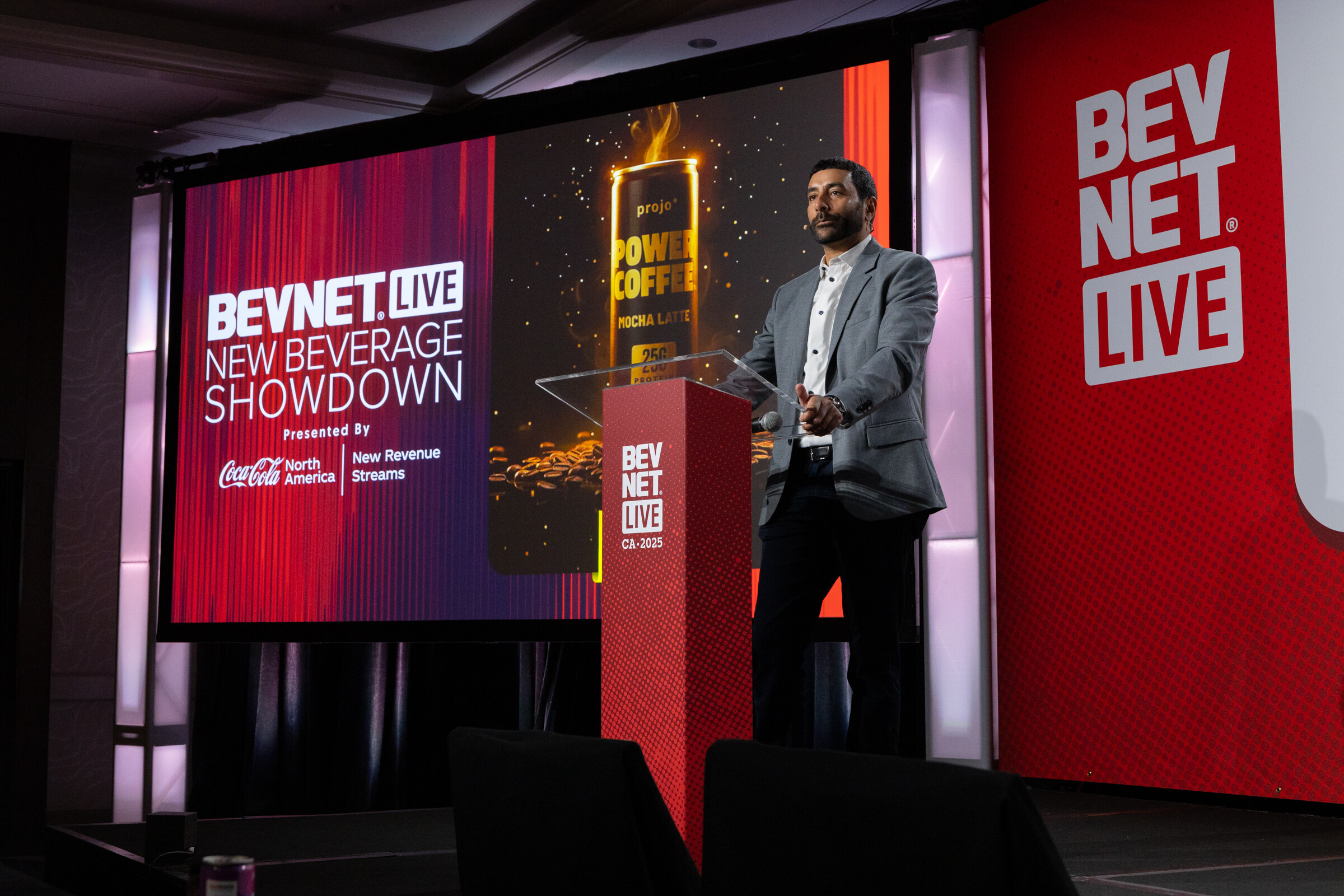 A man at the podium stands beside a Power Coffee slide on the showdown stage.