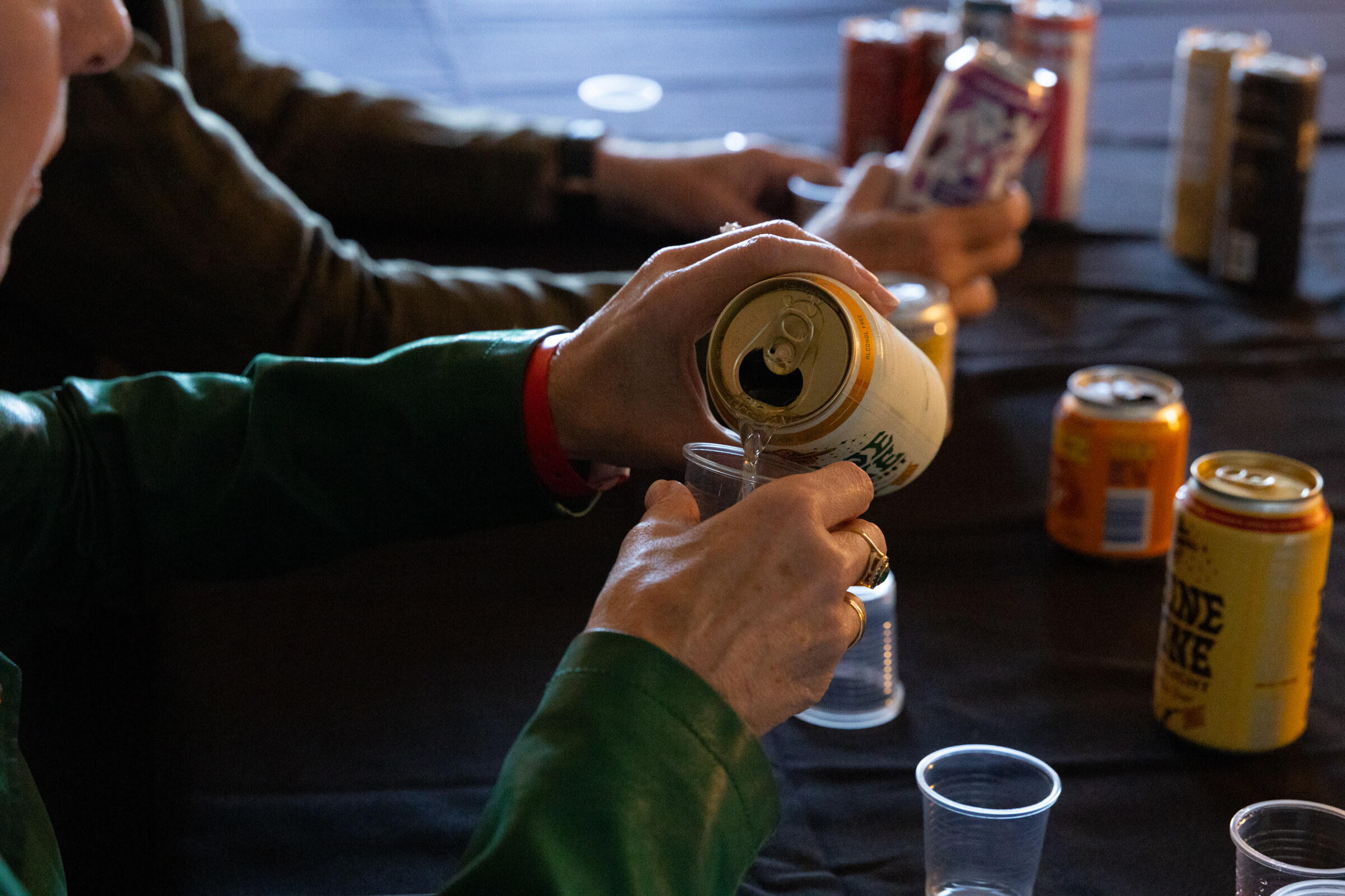 A hand pours a can into a cup beside other cans.