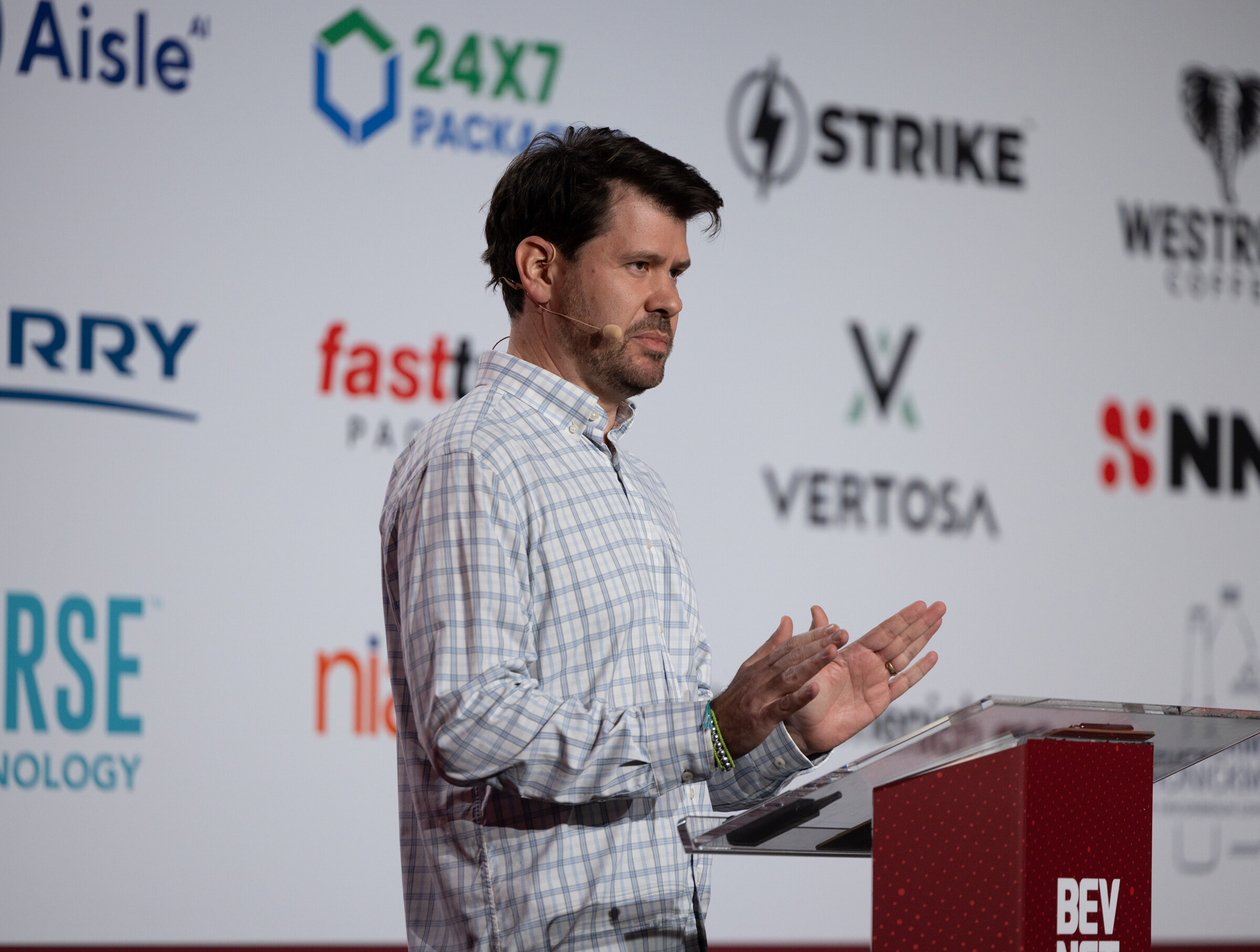 A man in a plaid shirt speaks at a podium on stage.