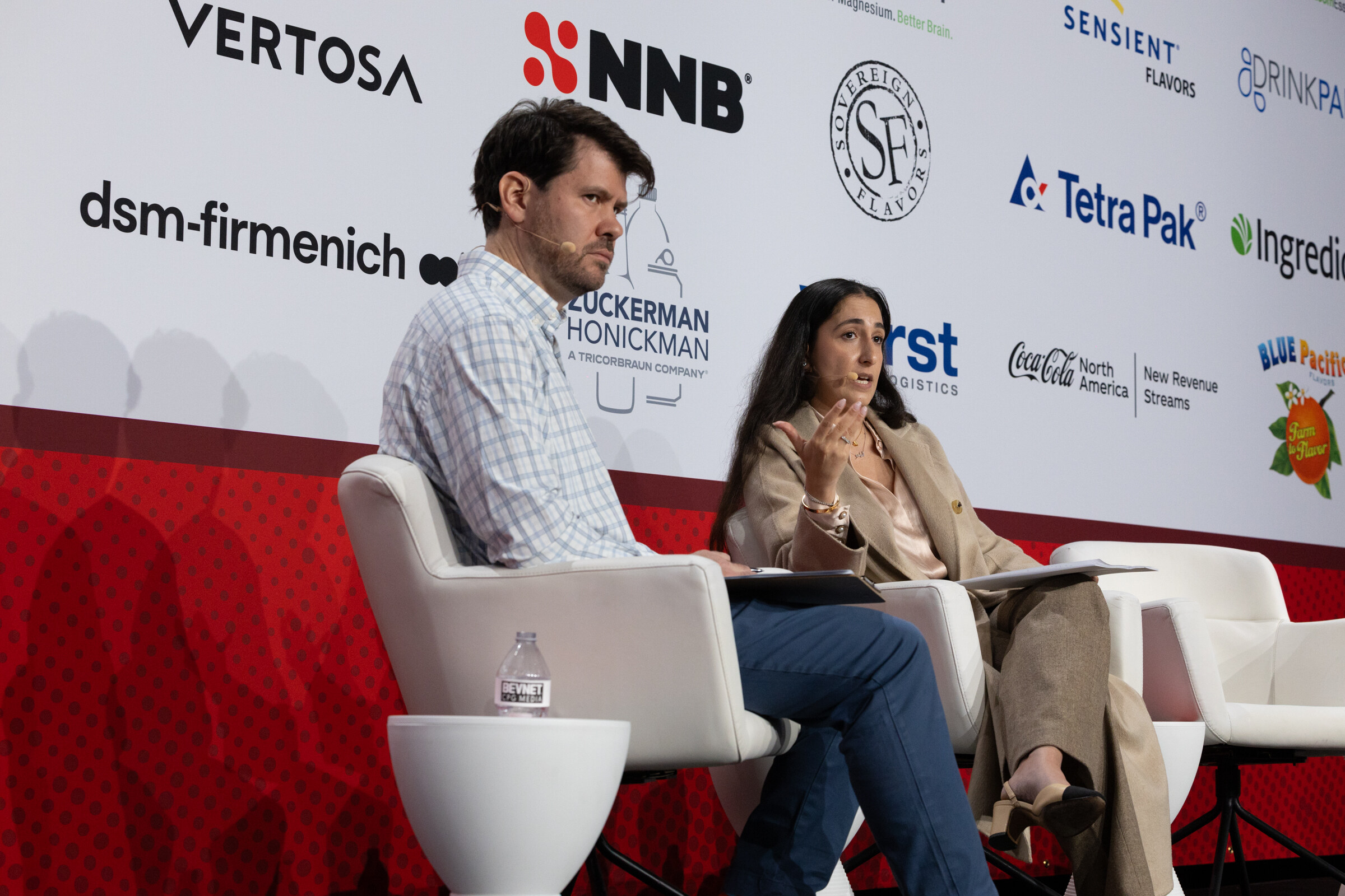 A woman in a dark top and a man in a plaid shirt sit on stage in conversation.