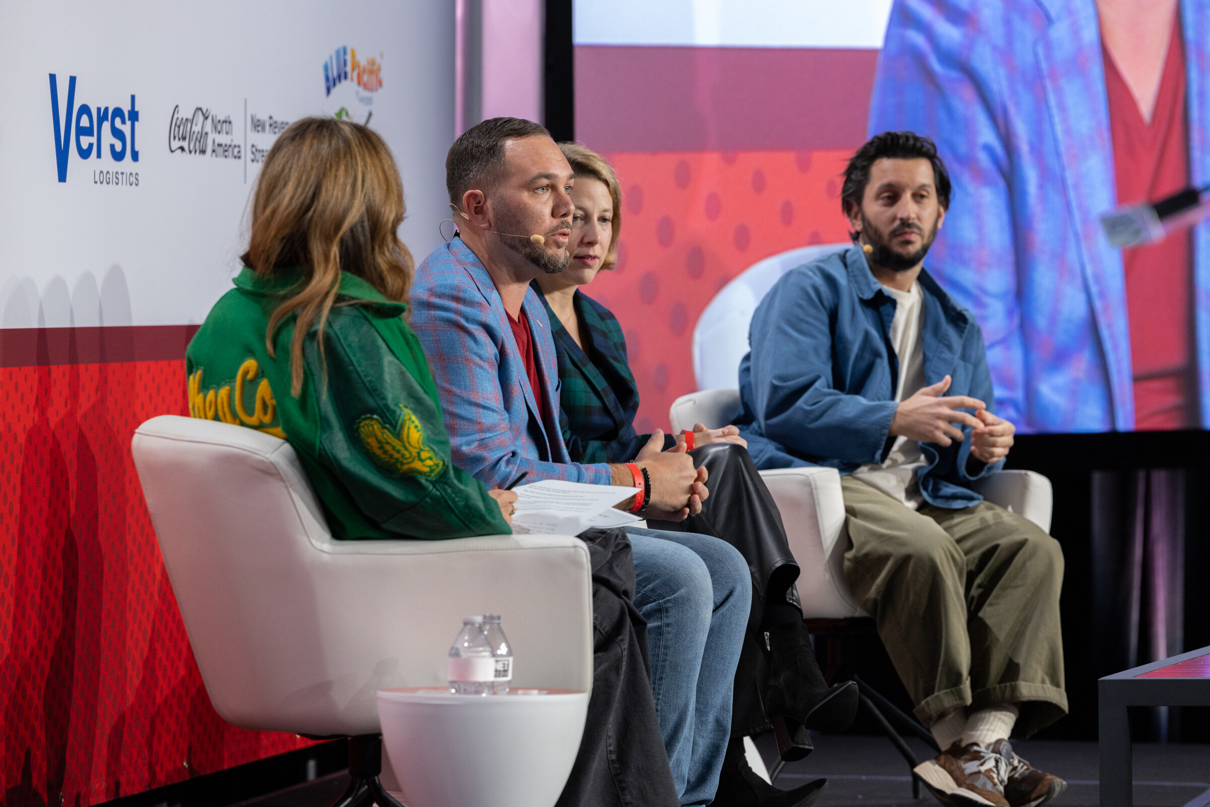 Three panelists in a green jacket, a blue jacket and a denim jacket sit on stage.