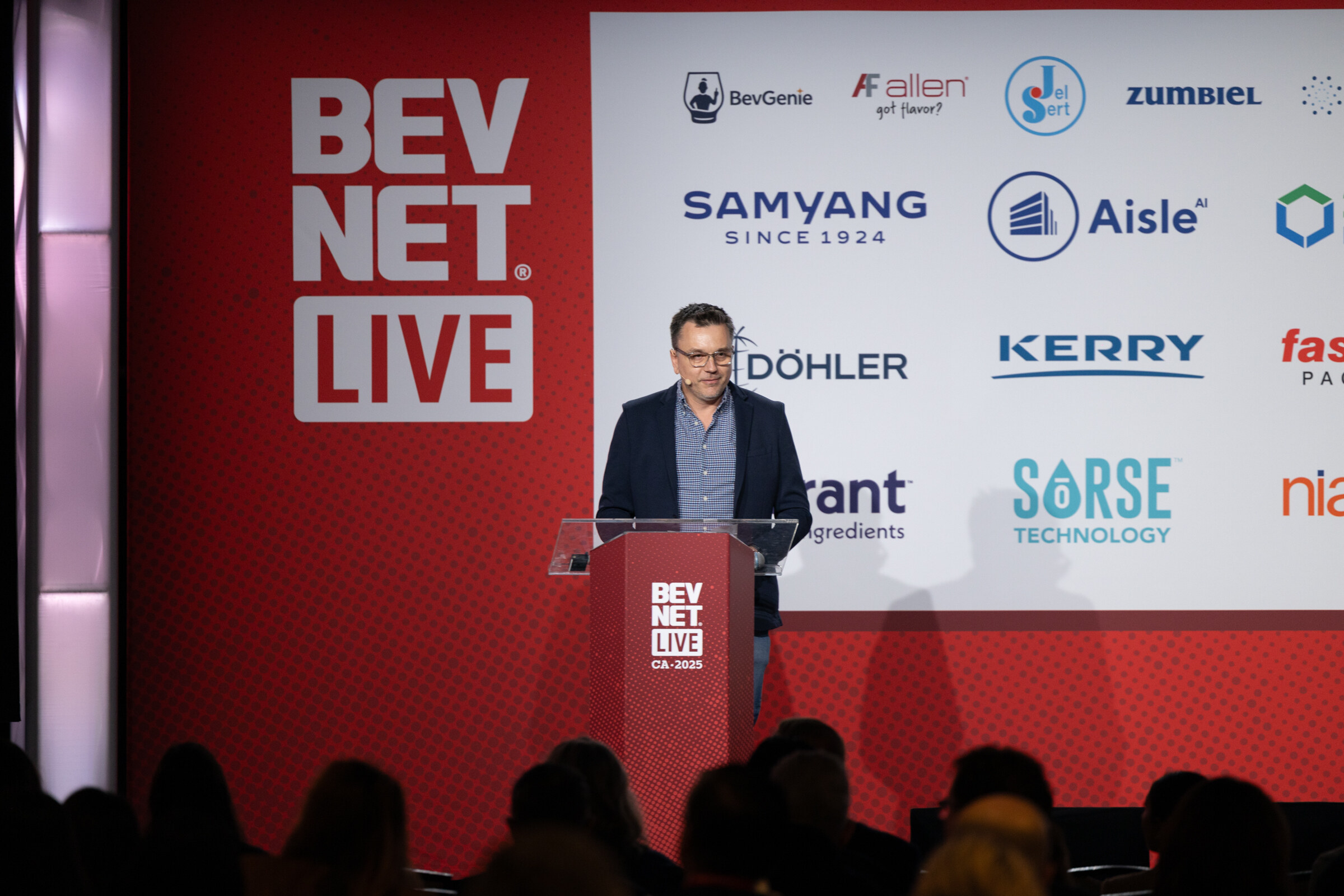 A man in a dark shirt speaks at a podium in front of a BevNET Live backdrop.