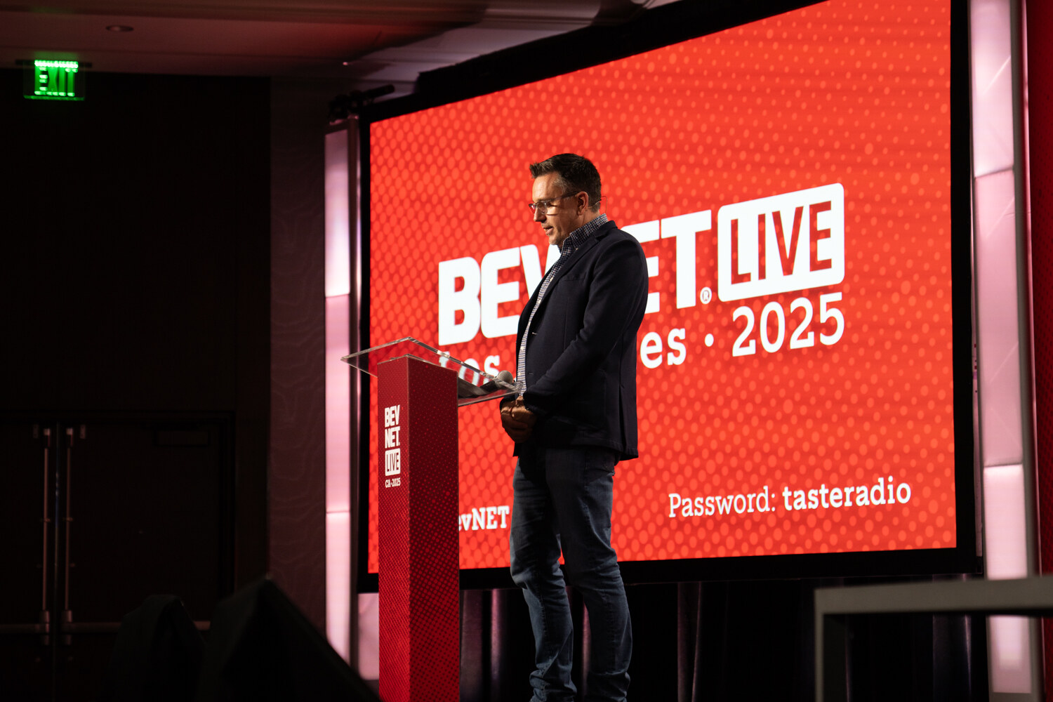 A man at the podium speaks in front of a red BevNET Live screen.