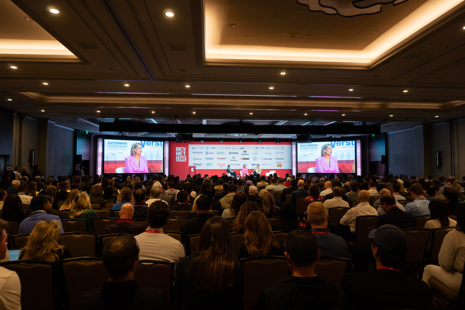 A wide shot of a full ballroom with screens at the front.