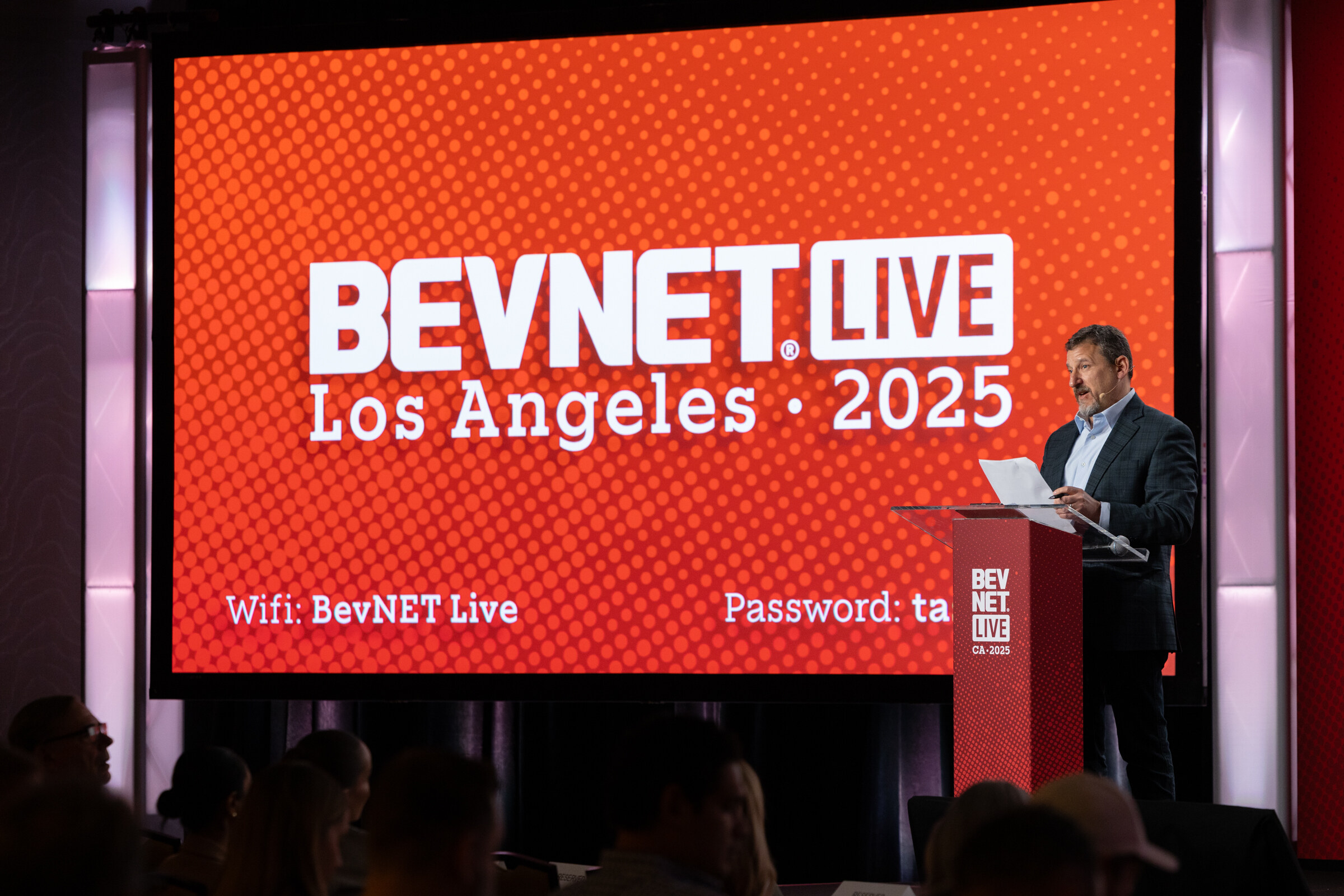 A man in a dark blazer stands at a podium before a BevNET Live Los Angeles 2025 screen.