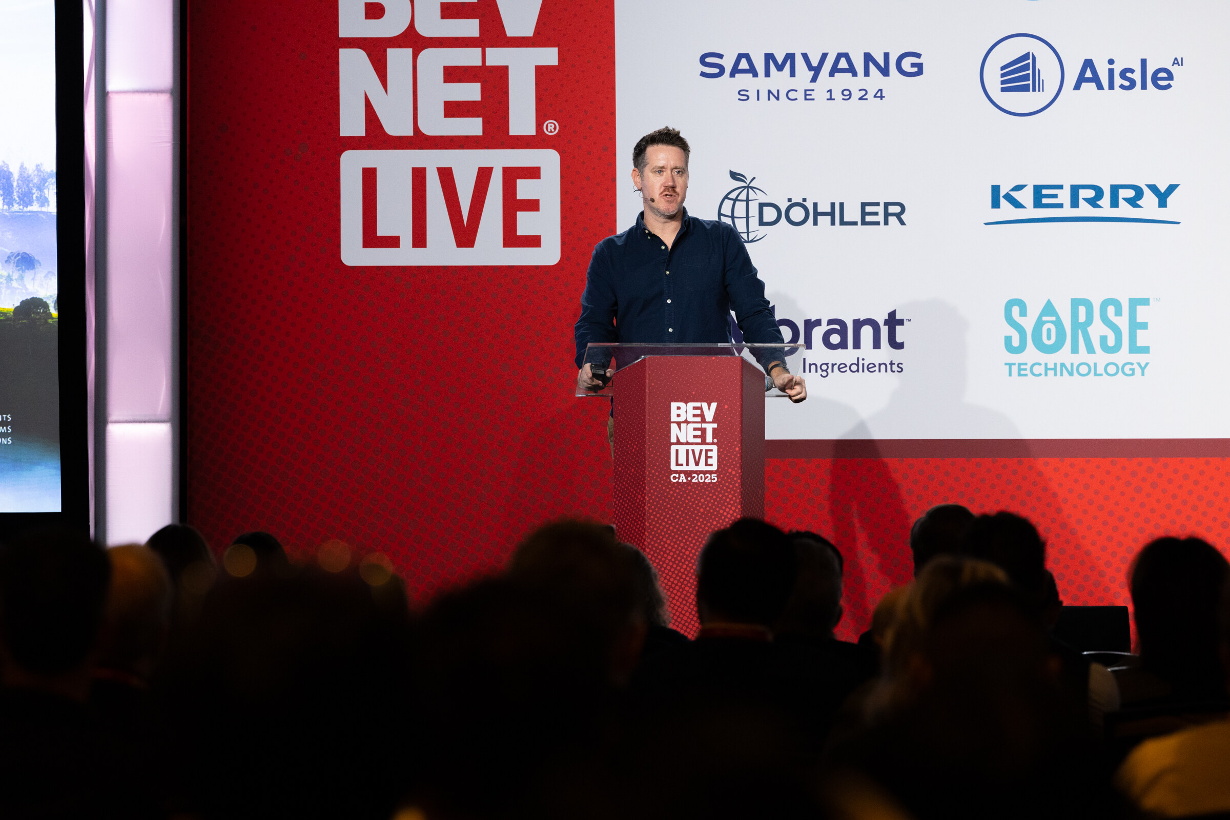 A man in a dark shirt speaks at a lectern in front of a BevNET Live backdrop.