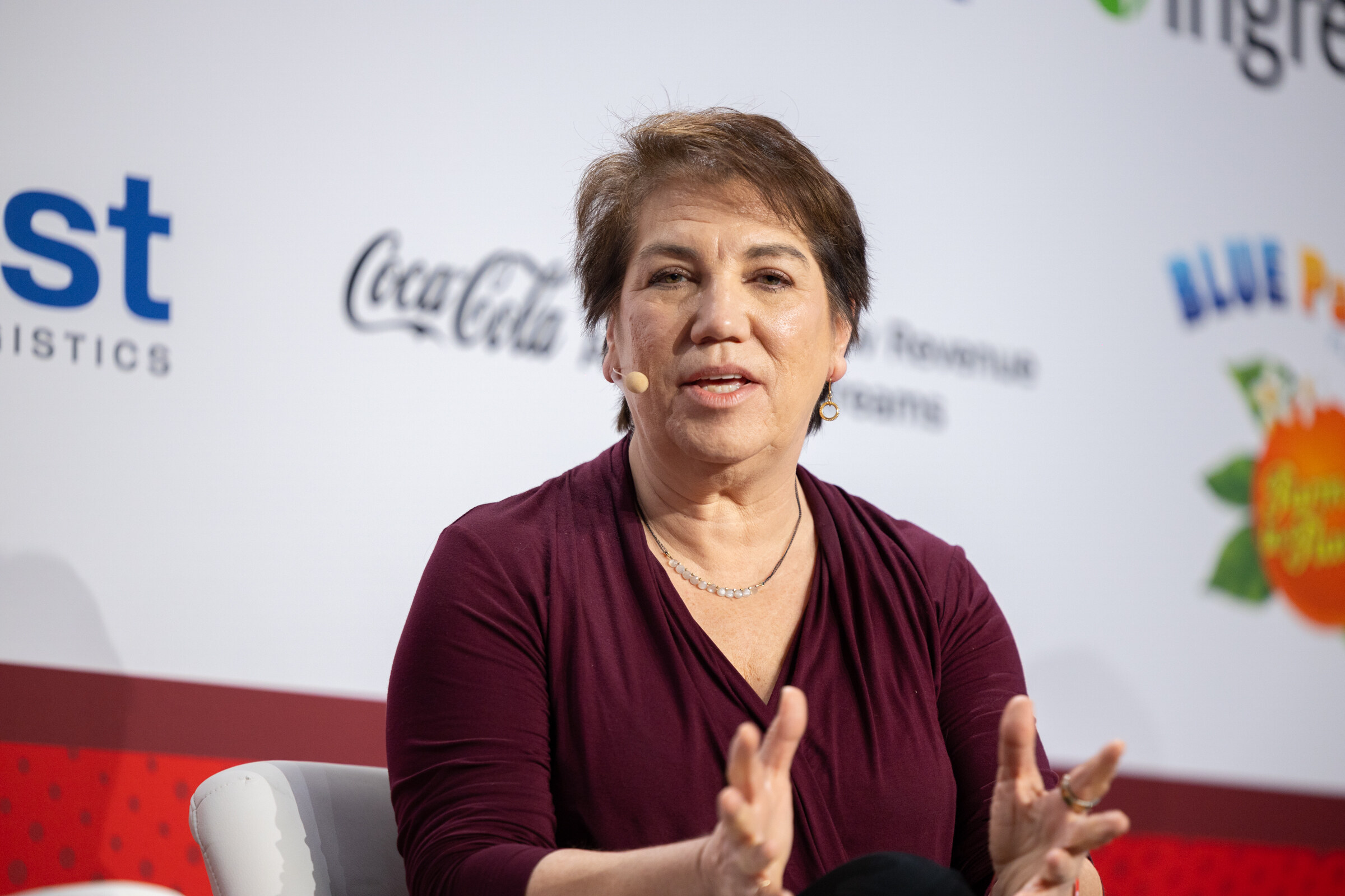 A woman in a burgundy top speaks while seated on stage.