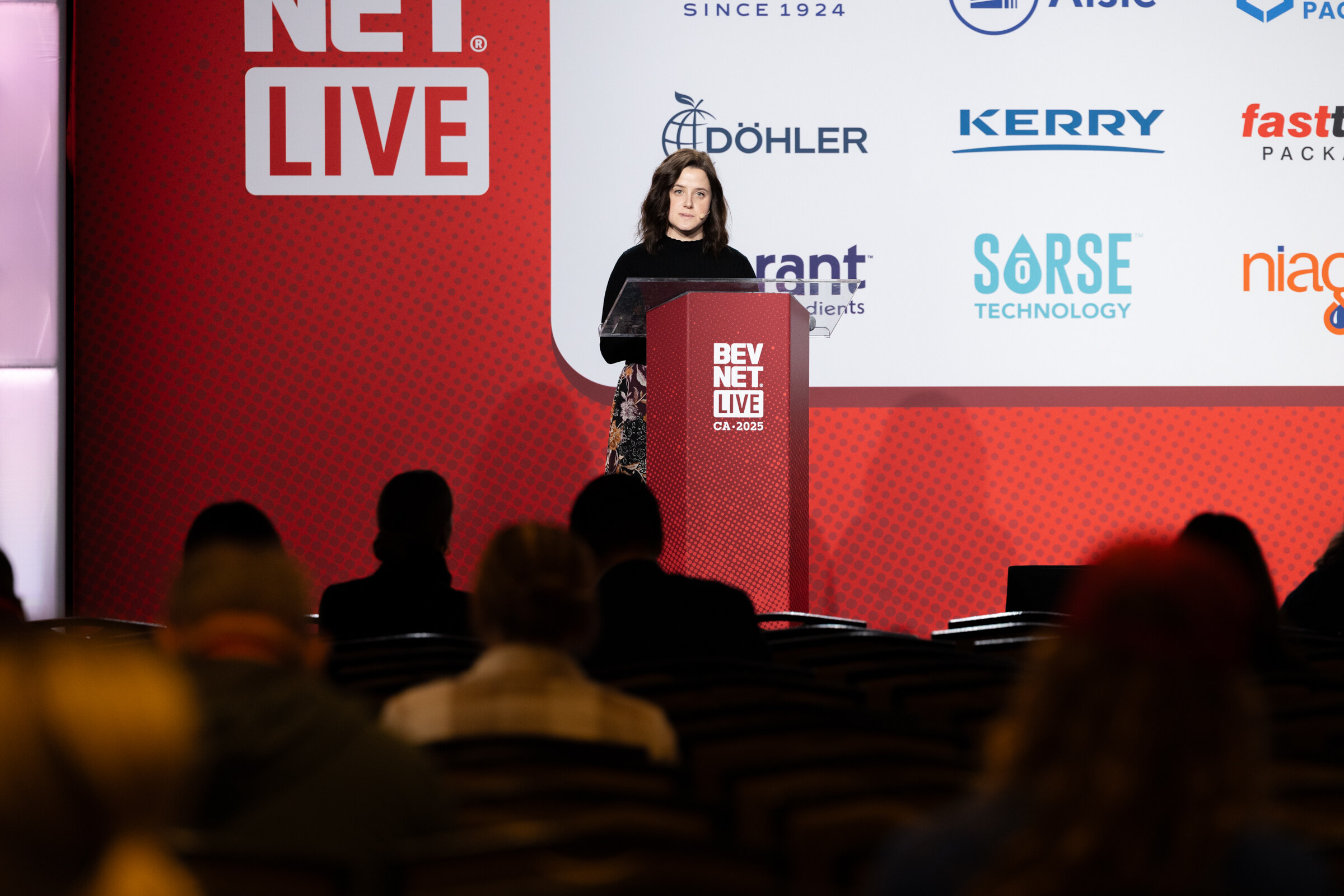 A woman speaks at the podium on stage in front of an audience.