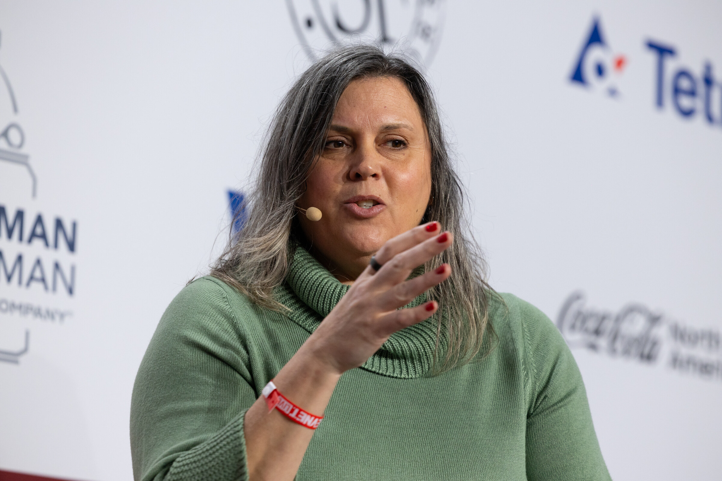 A woman in a green turtleneck speaks and gestures on stage.