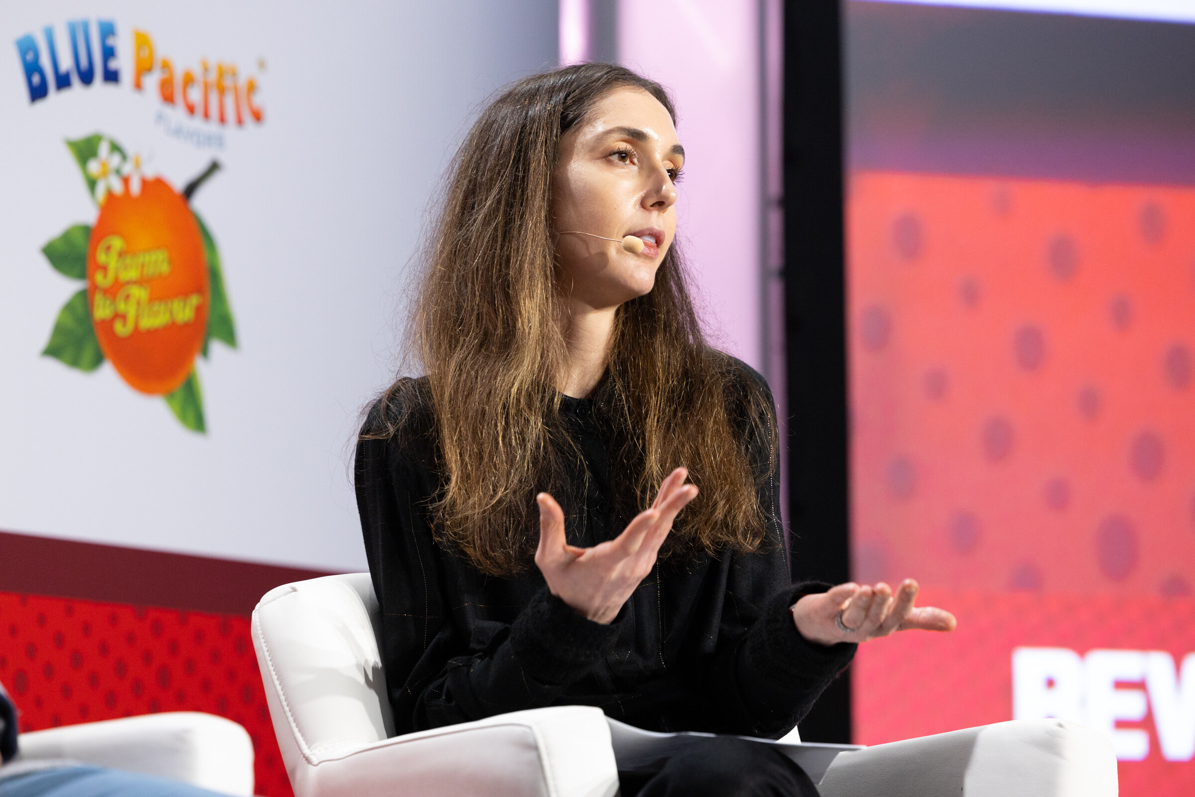 A woman with long dark hair speaks while seated on stage.