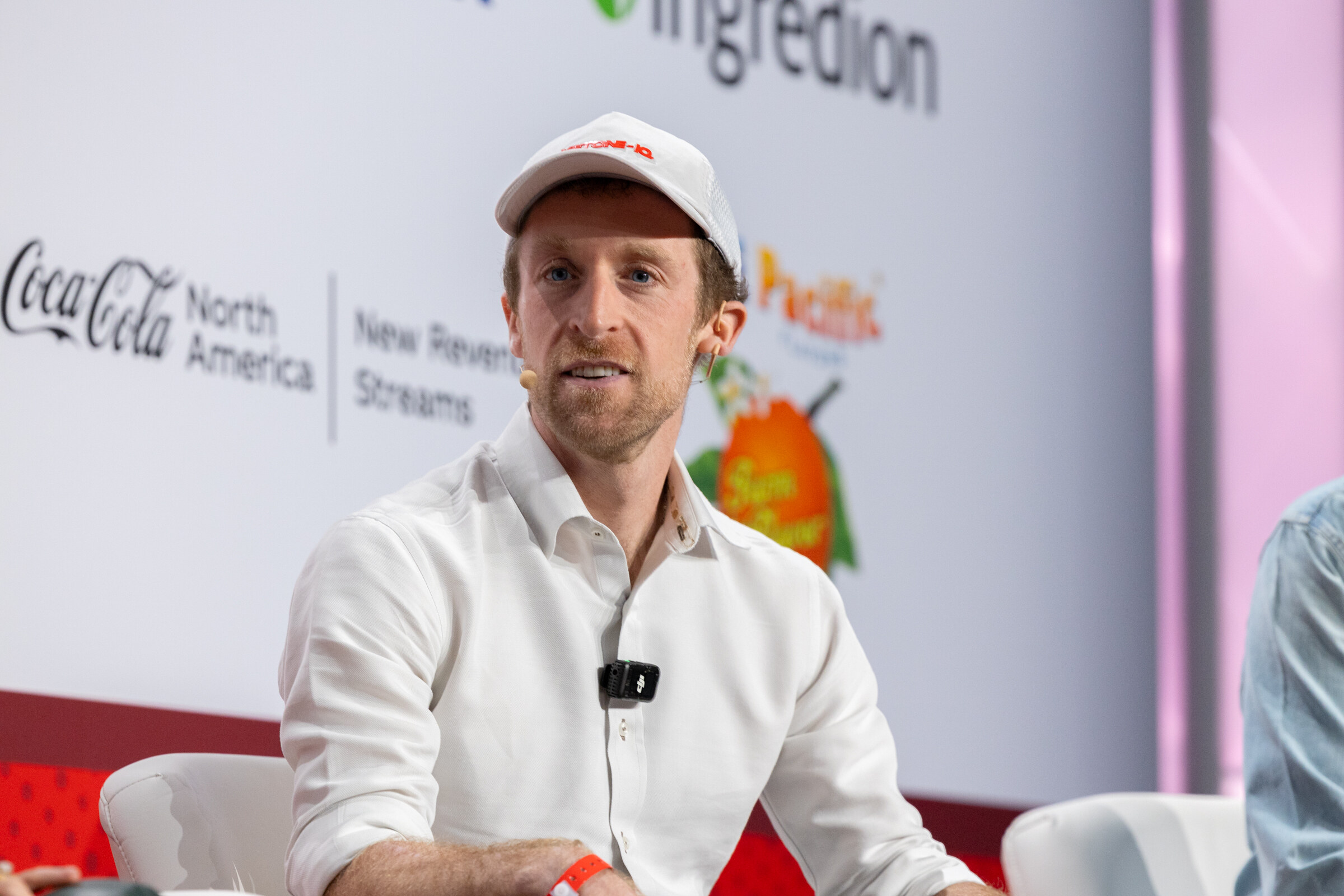 A man in a white shirt gestures while seated on stage.