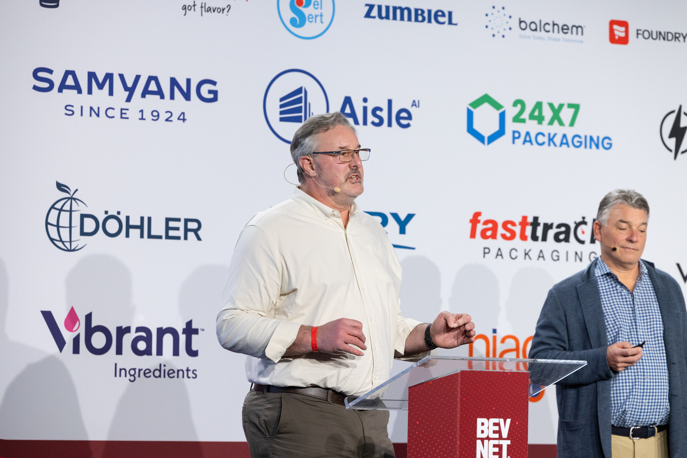Two men stand on stage in front of the BevNET Live backdrop.