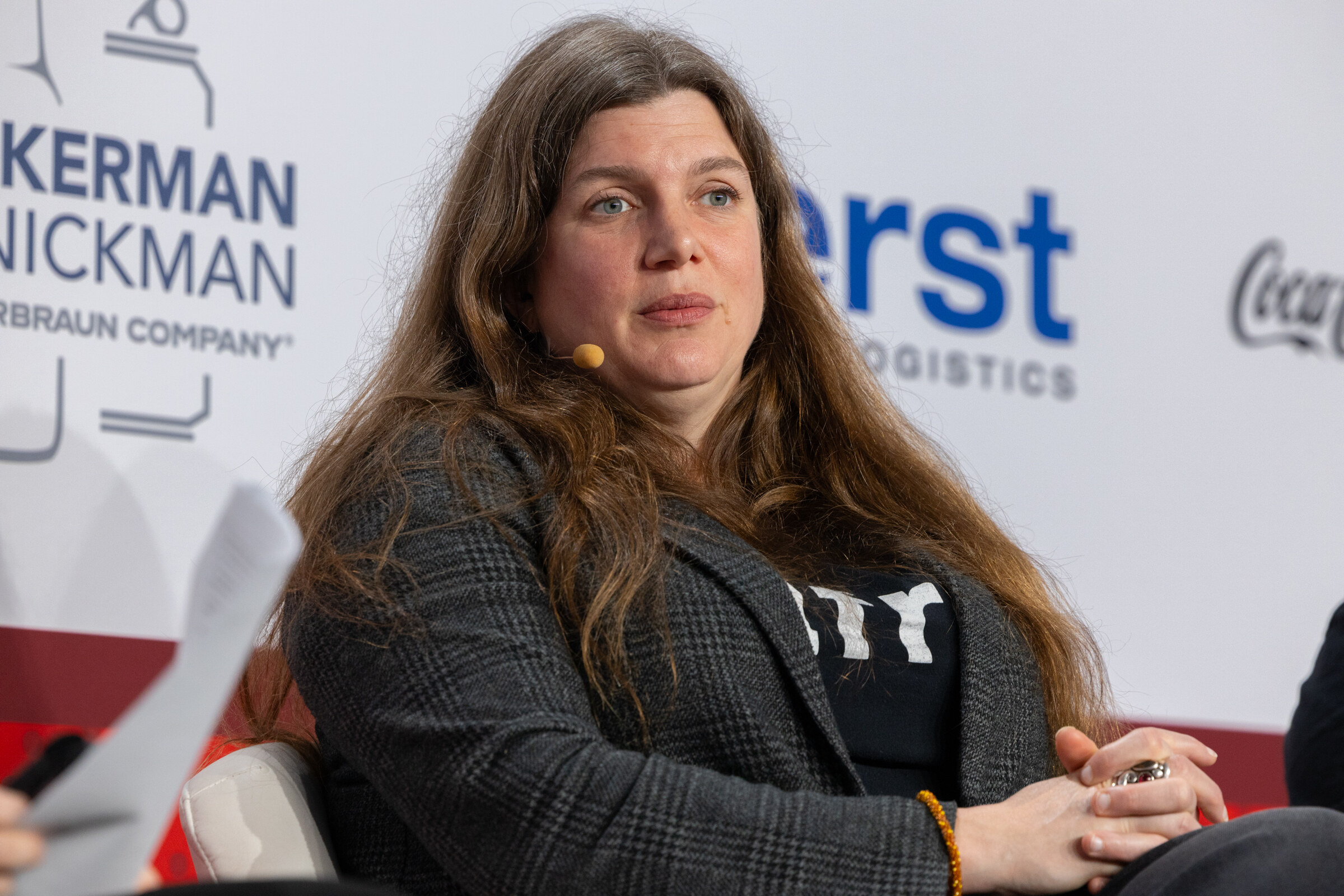 A woman in an INFRA shirt sits on stage in front of a sponsor wall.