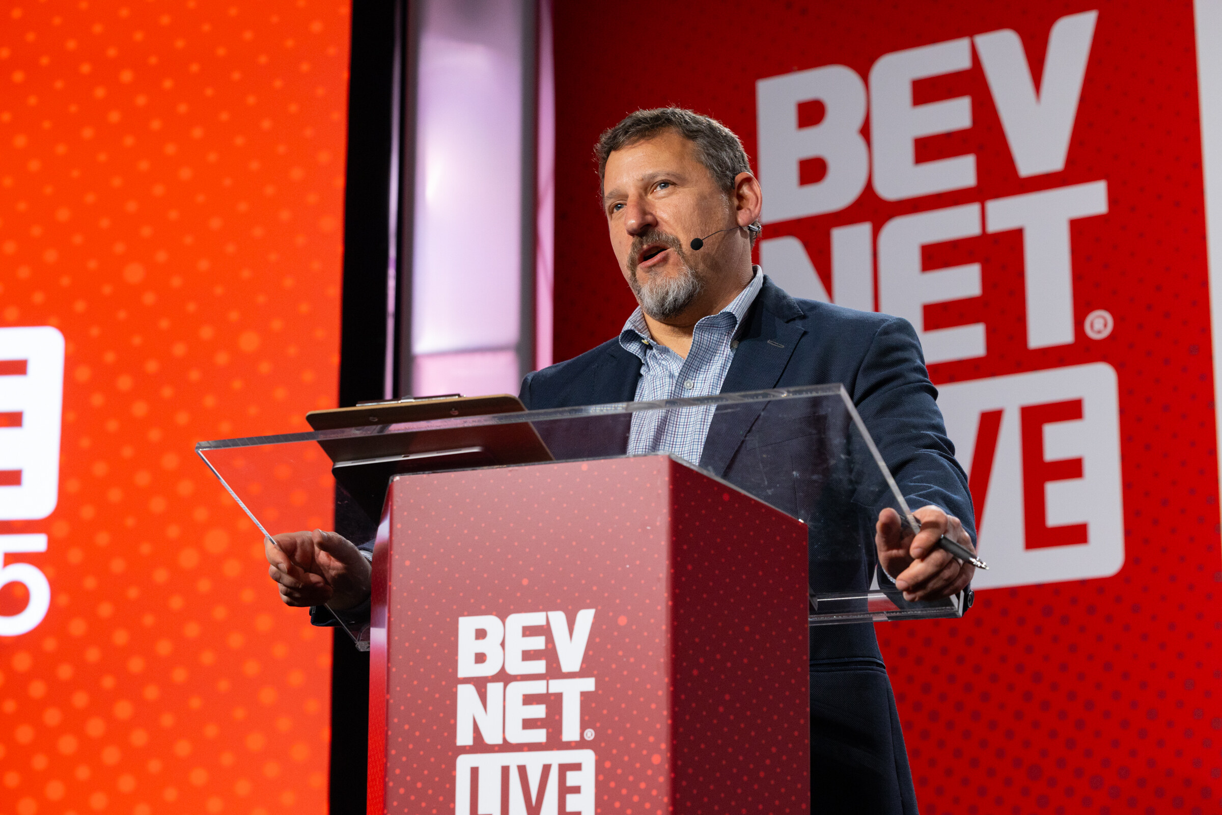 A man in a navy blazer speaks at the BevNET Live lectern.