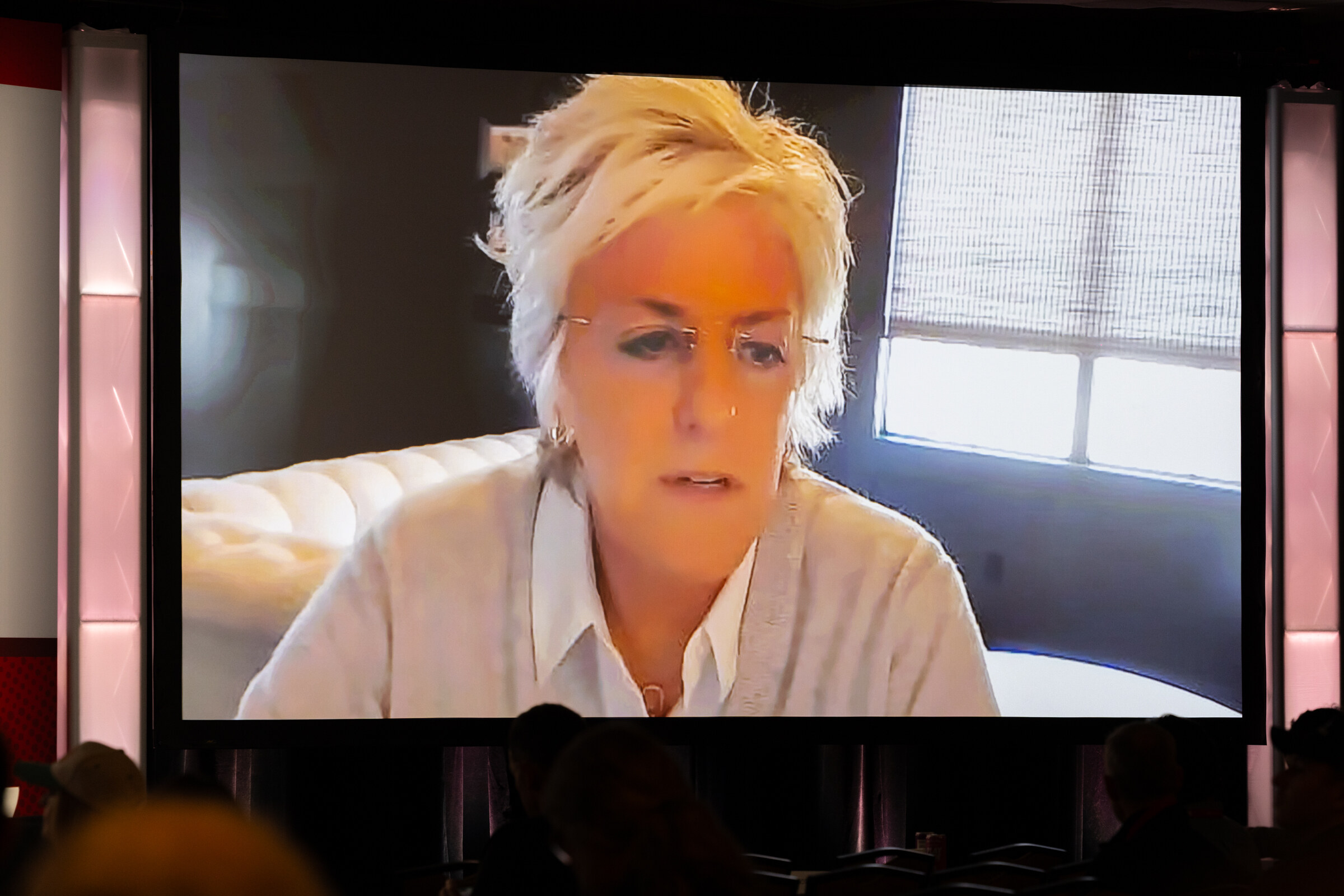 A woman appears on the large ballroom screen via video.