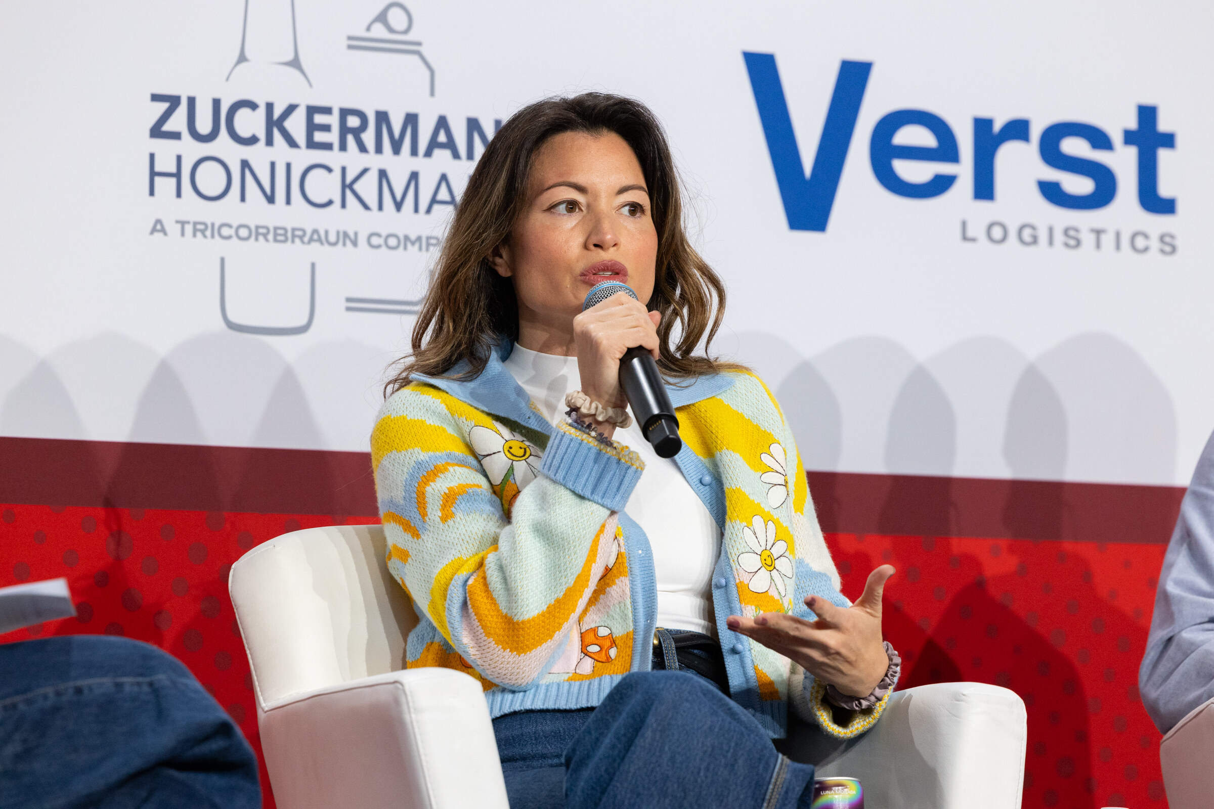 A woman in a colorful patterned jacket speaks into a microphone.