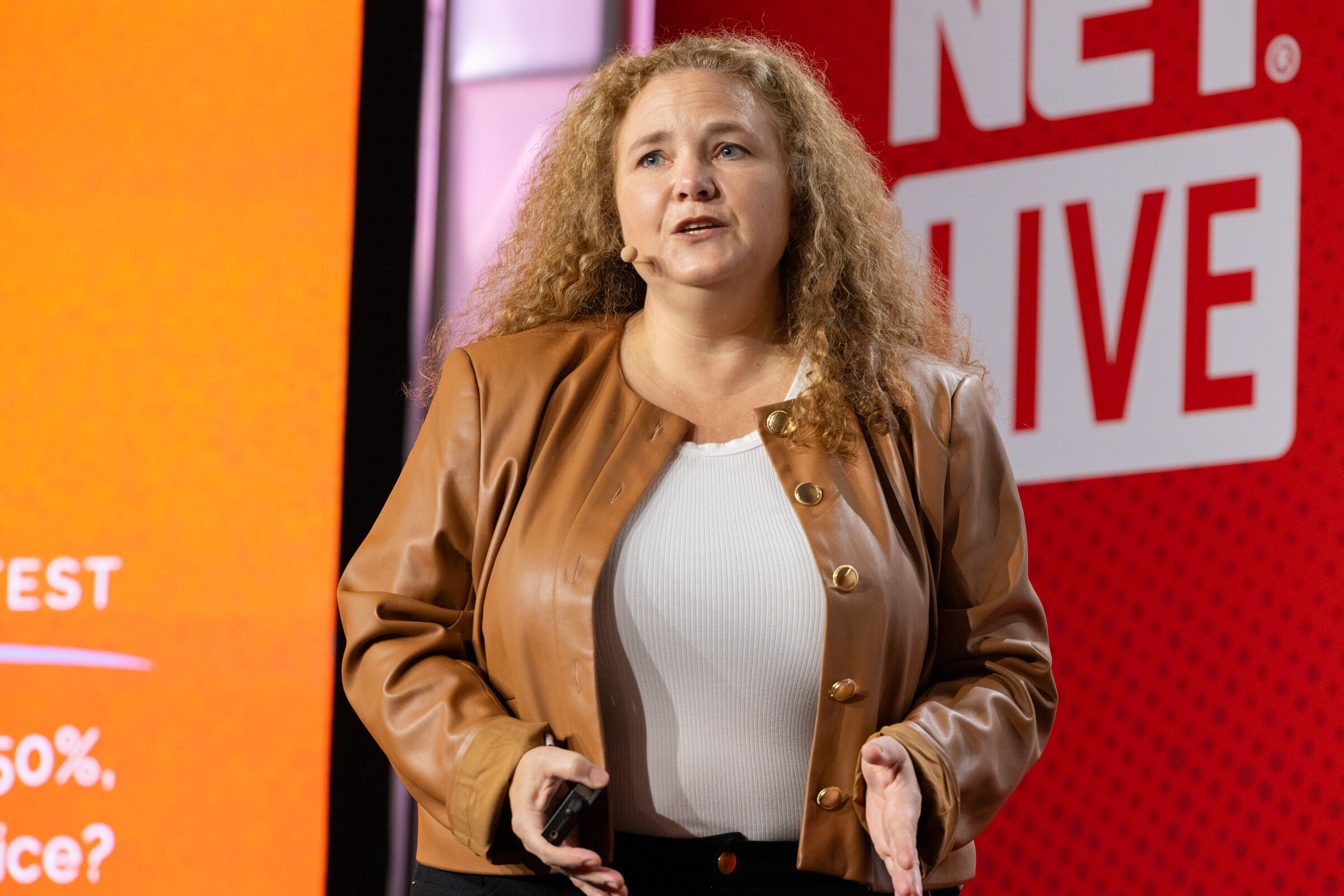 A woman in a tan jacket speaks in front of an orange slide.