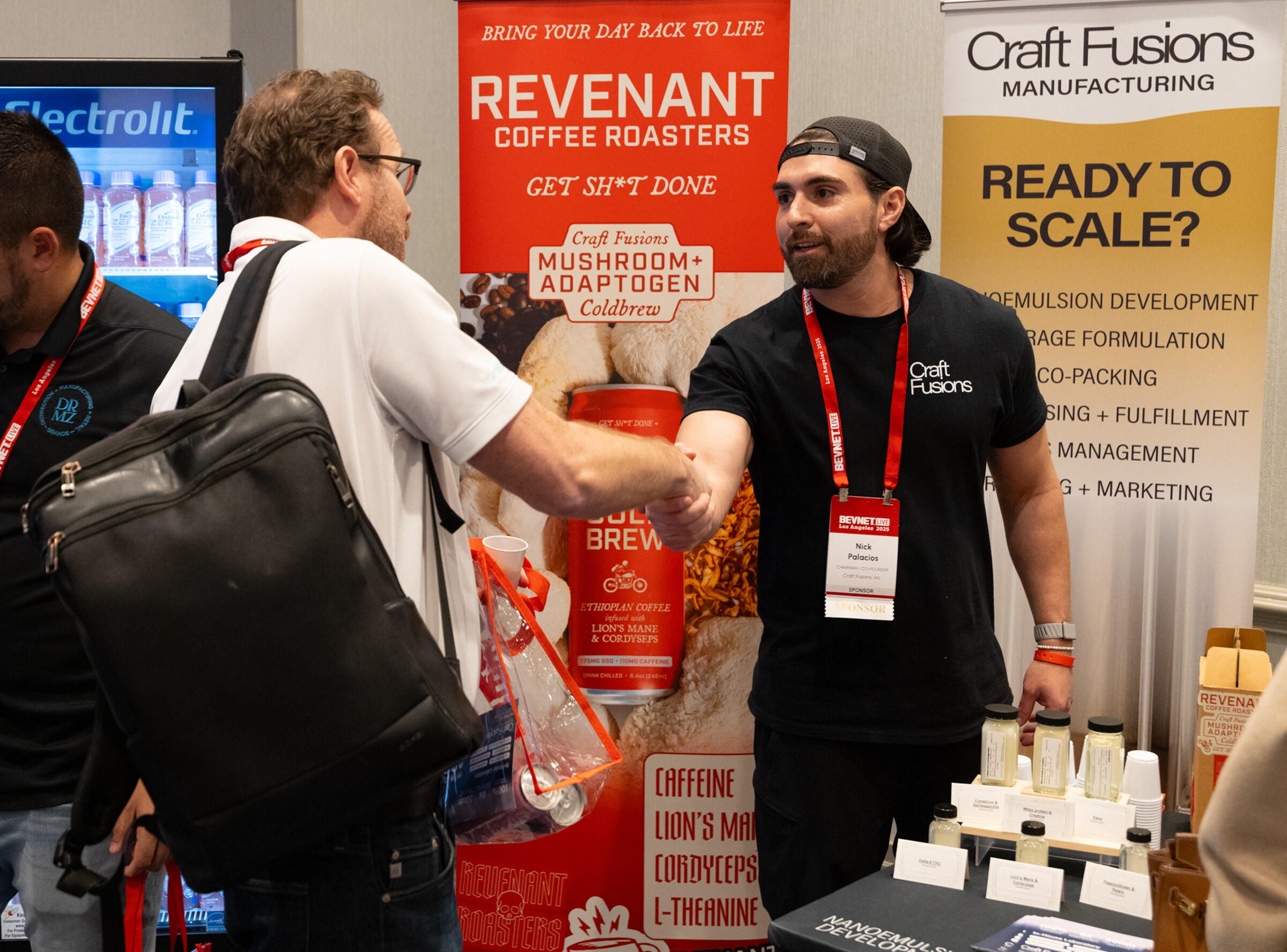 A man with a backpack shakes hands with a Craft Fusions rep at a booth.