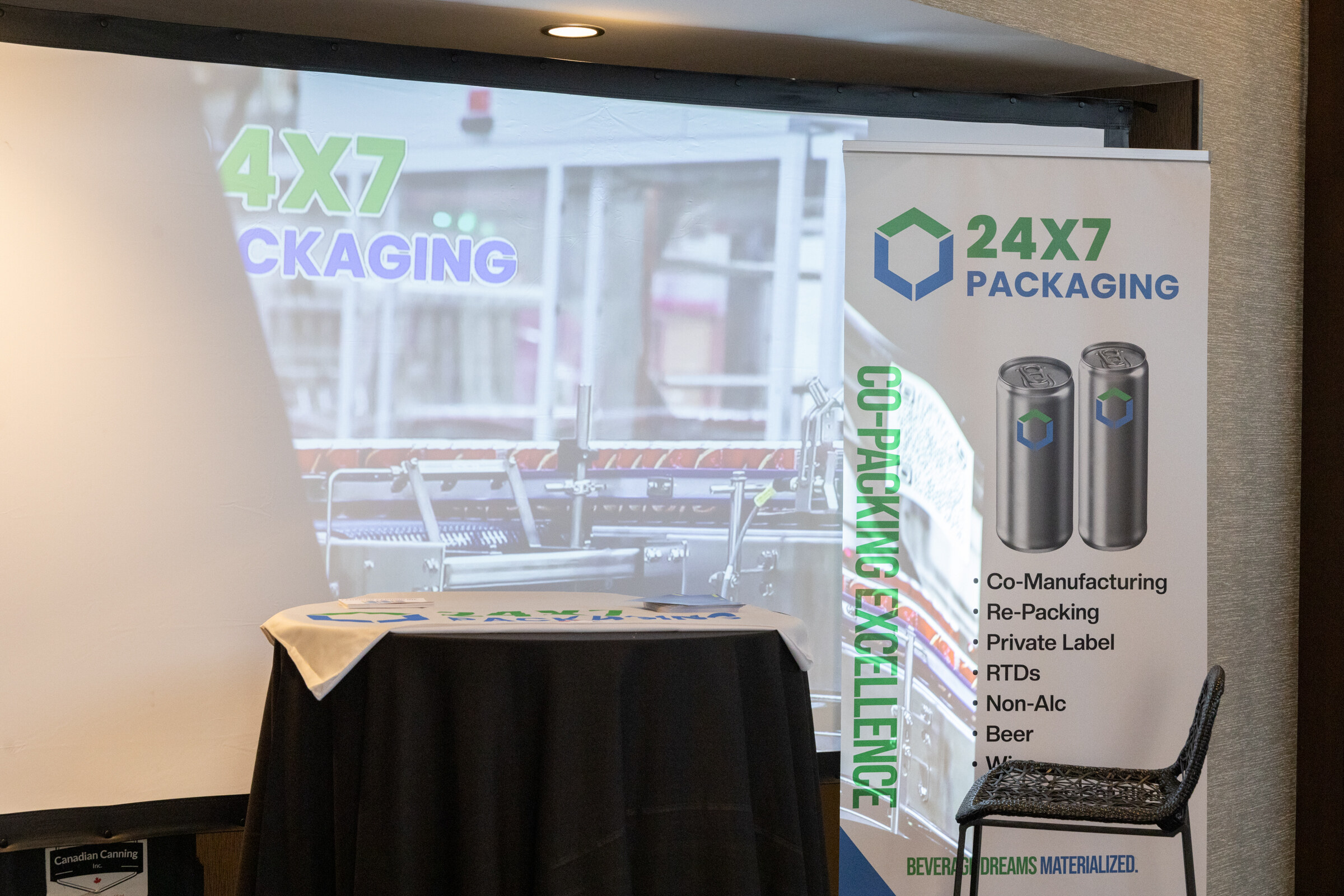 A black table in front of a 24/7 Packaging banner and screen.