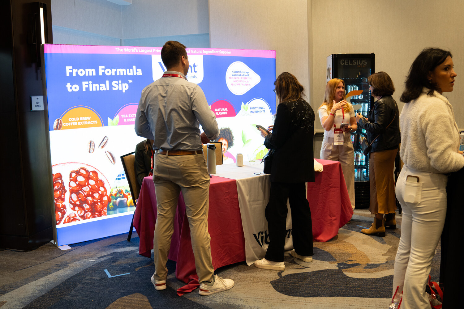 Attendees talk at a lit Vibrant booth with a red tablecloth.