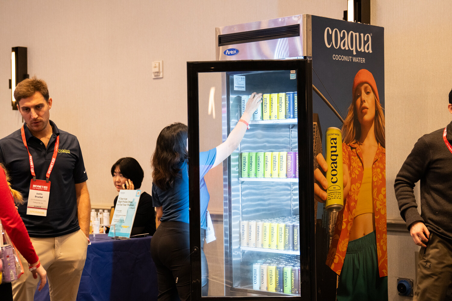 Attendees stand near a lit fridge with a Coaqua coconut water graphic.