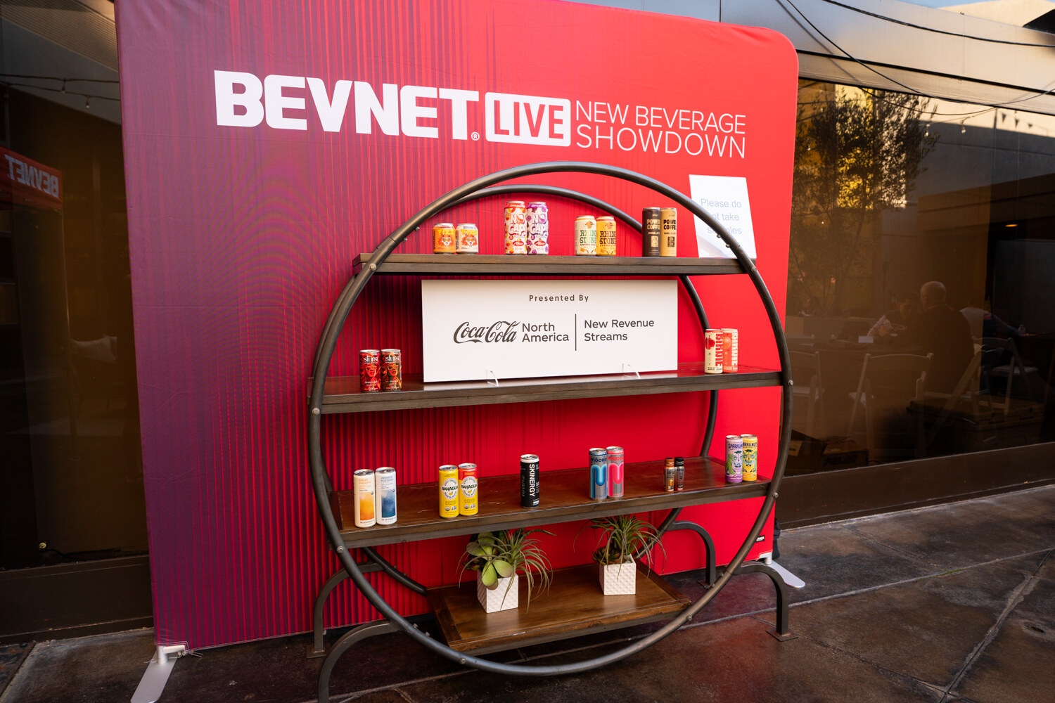 A circular red shelf holds cans in front of a New Beverage Showdown backdrop.