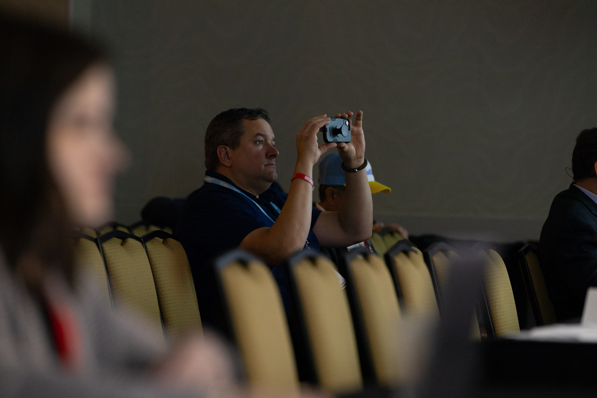 An attendee photographs the stage with a phone while others listen.