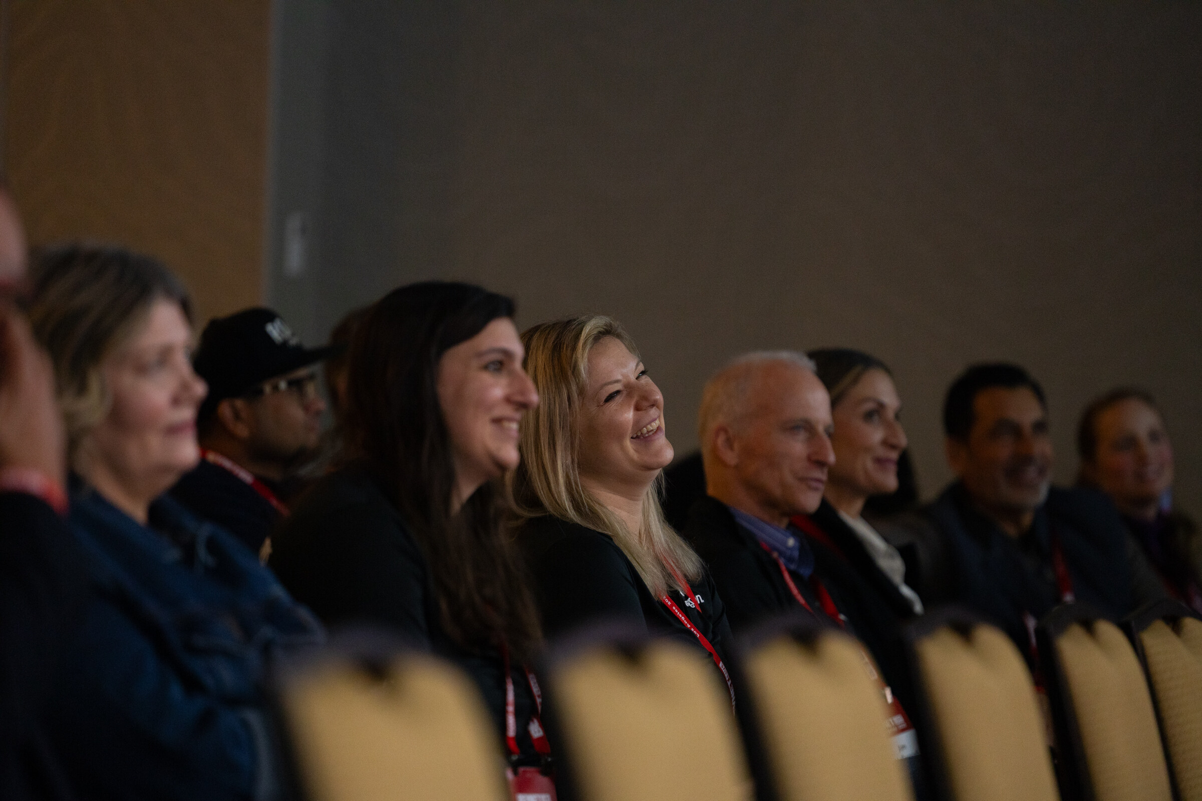 Attendees in a row of chairs laugh and watch a speaker.