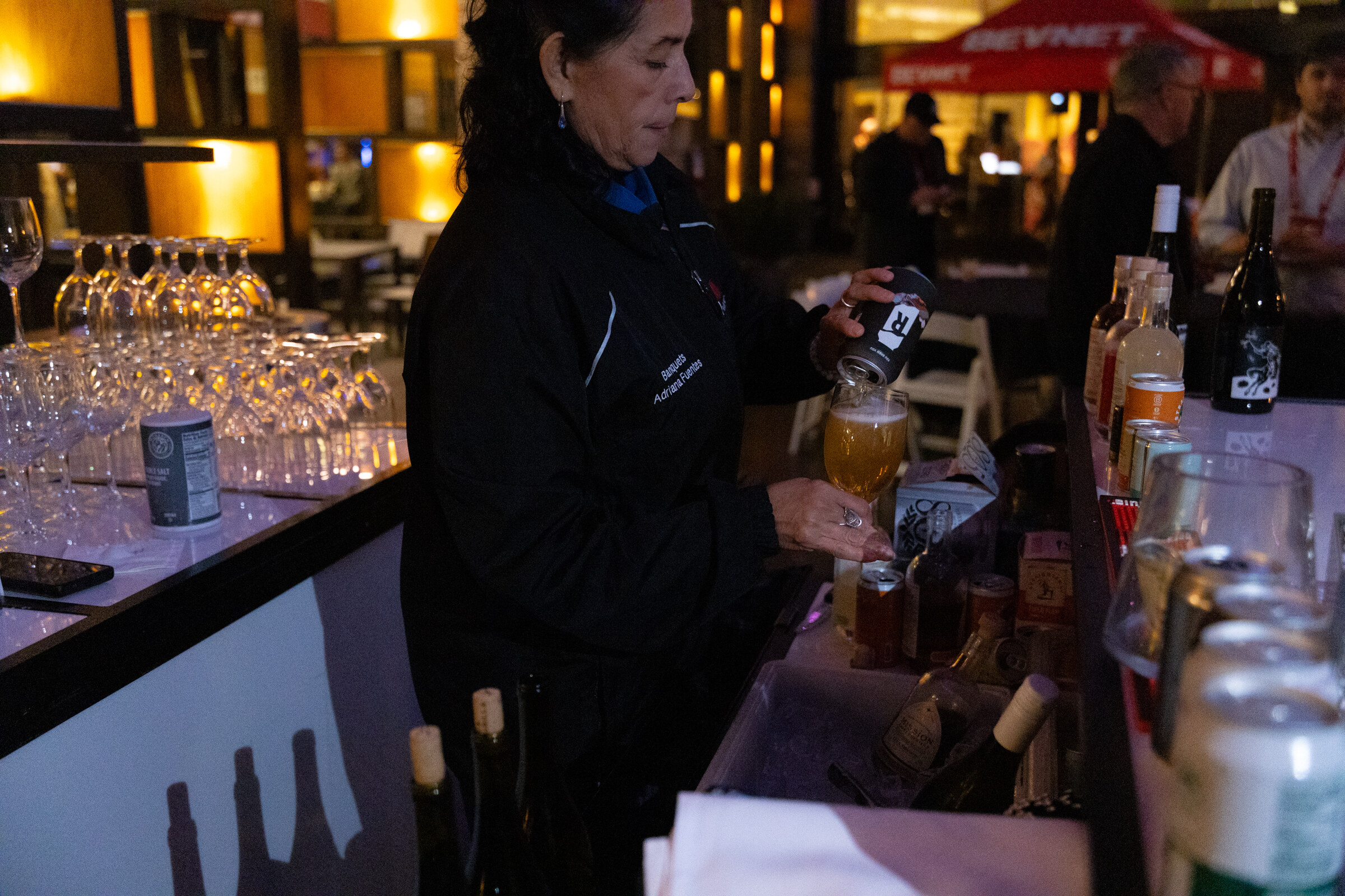 A bartender pours a drink behind a bar with rows of glasses.