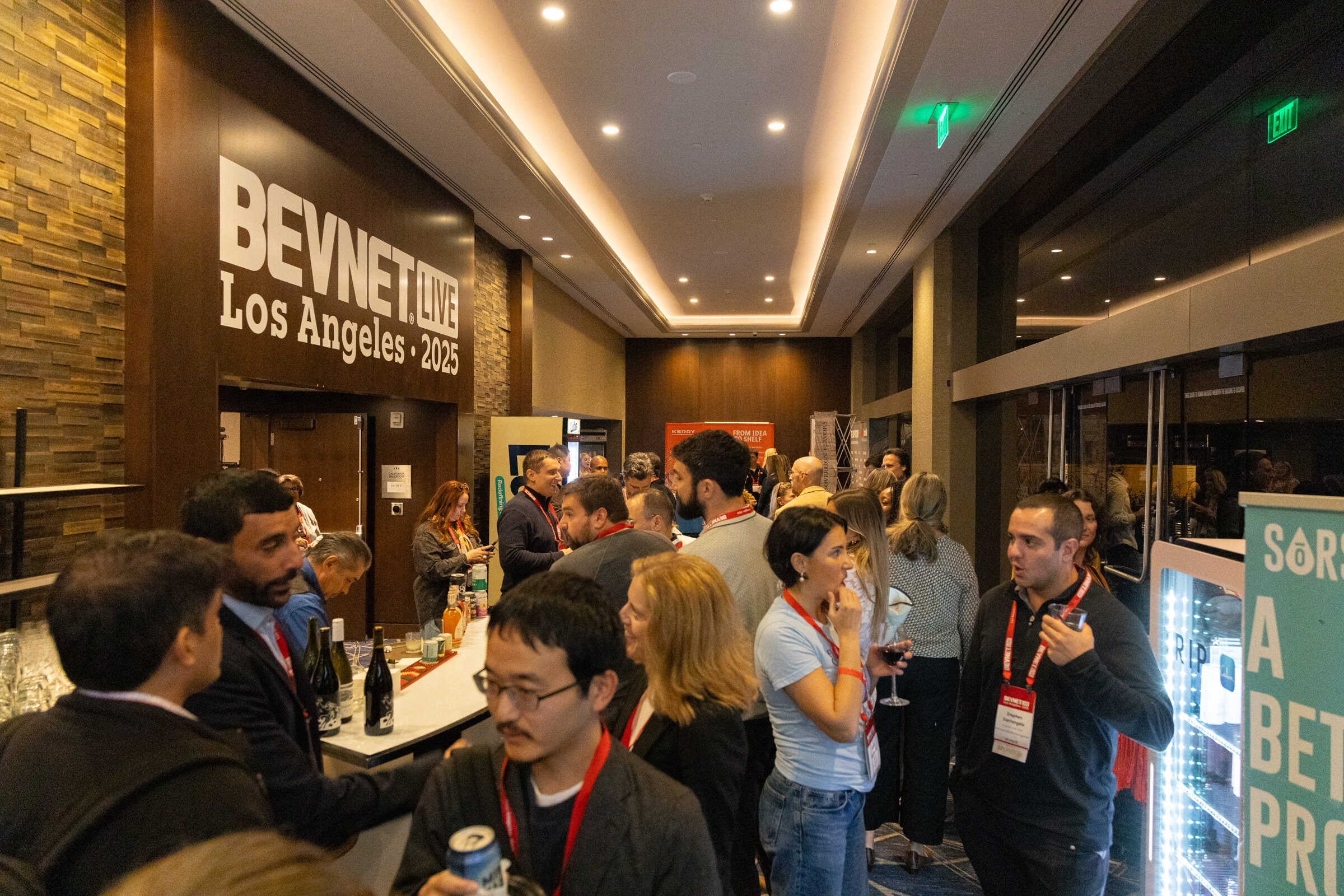Attendees with lanyards talk and drink in a room with the BevNET Live sign.