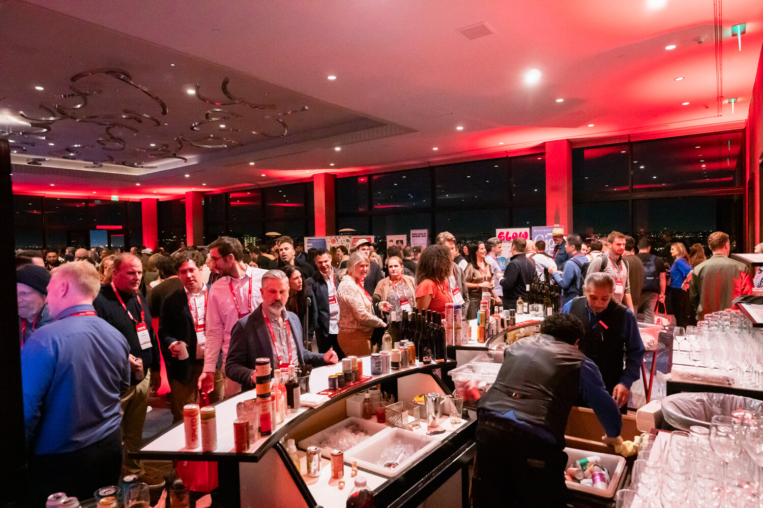 Attendees fill a red-lit party room with a bar on the left.