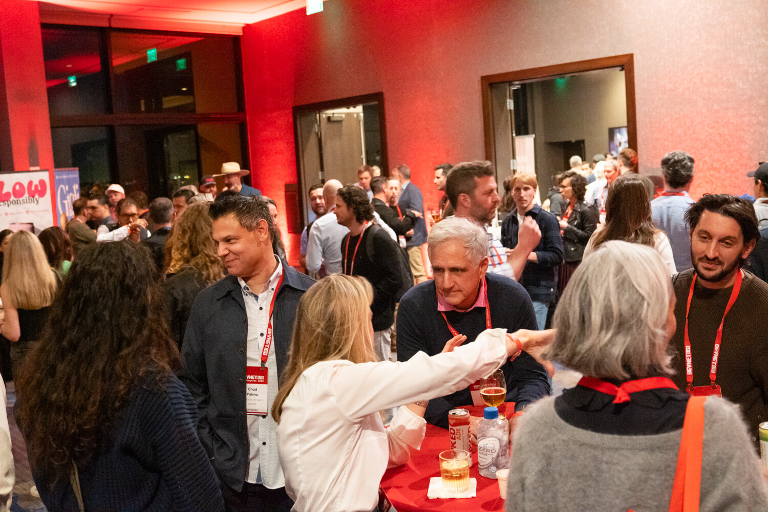 A group of attendees with lanyards chat around a table at the party.