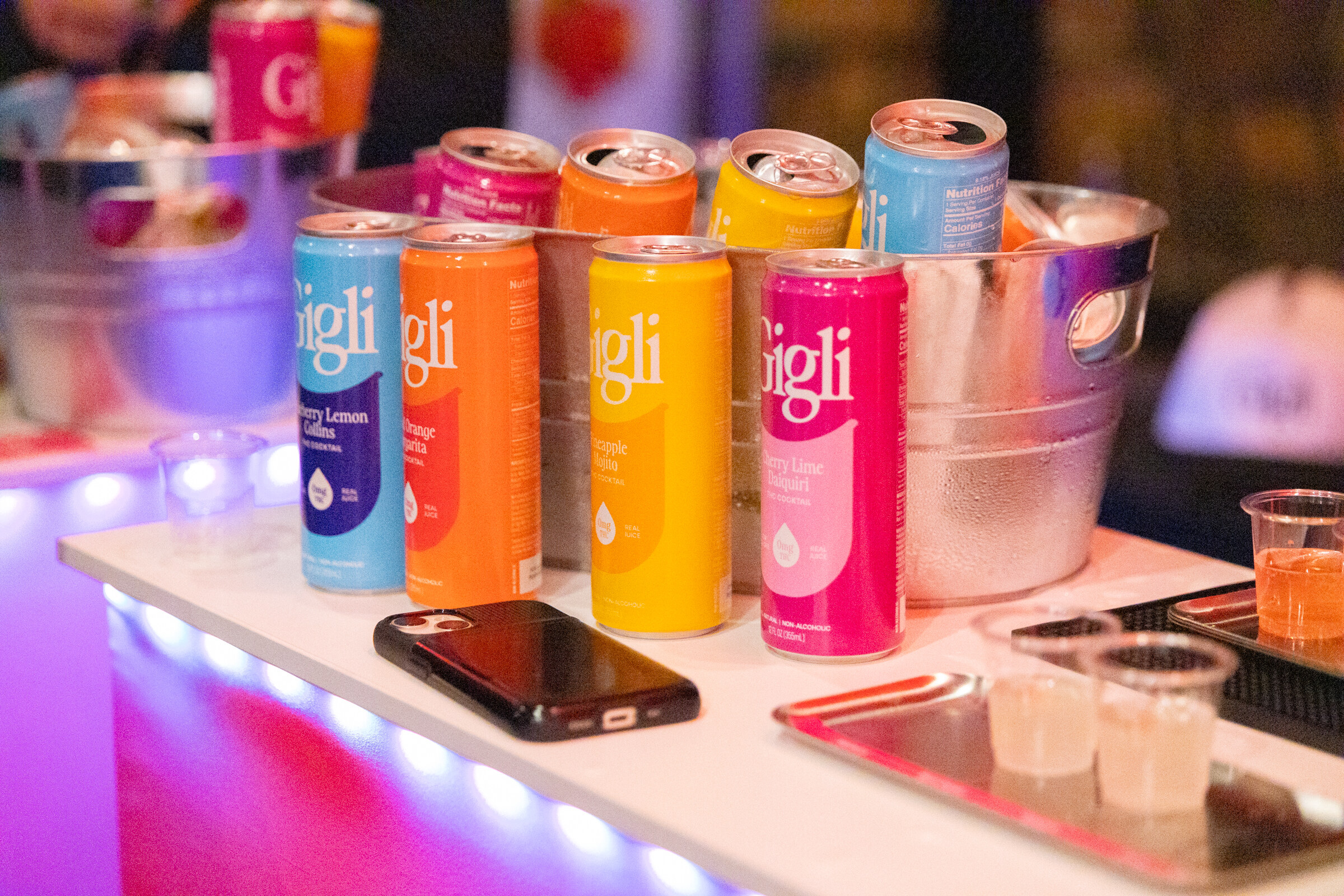Colorful Gigli cans stand in a bucket on a lit table.