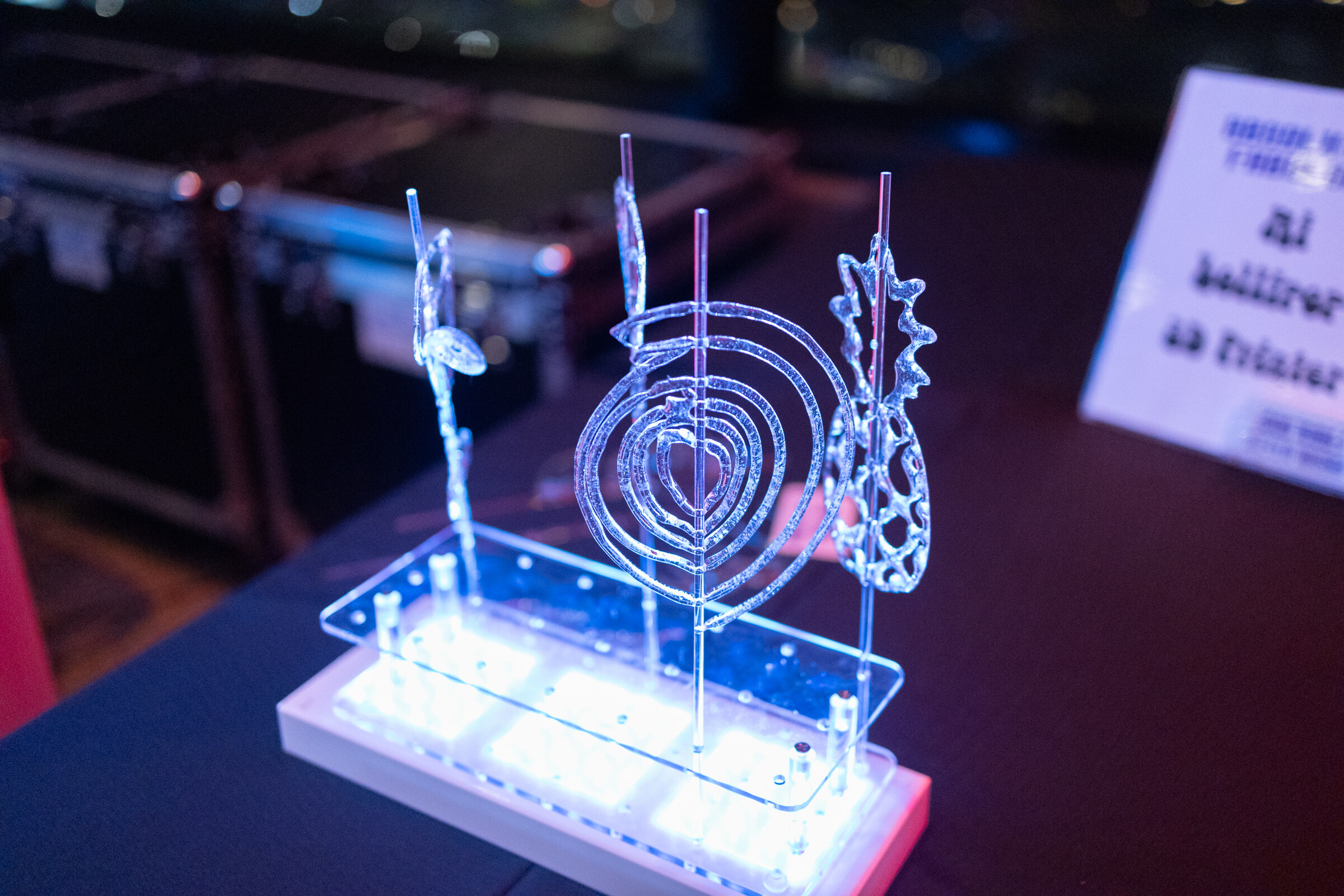 A lit acrylic display with hearts, a pineapple and swirls glows on a dark table.