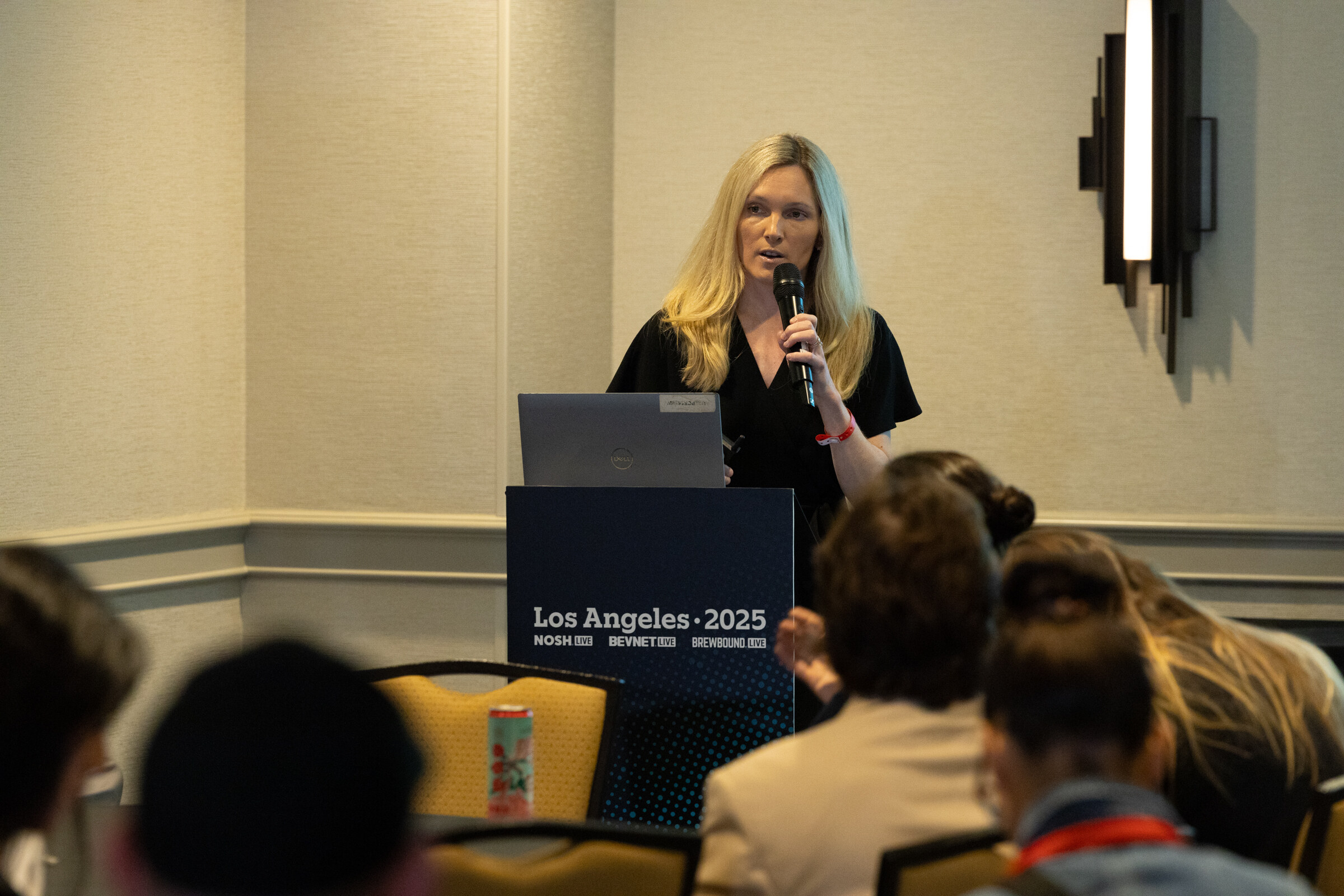 A woman with a microphone speaks at a lectern in a small meeting room.