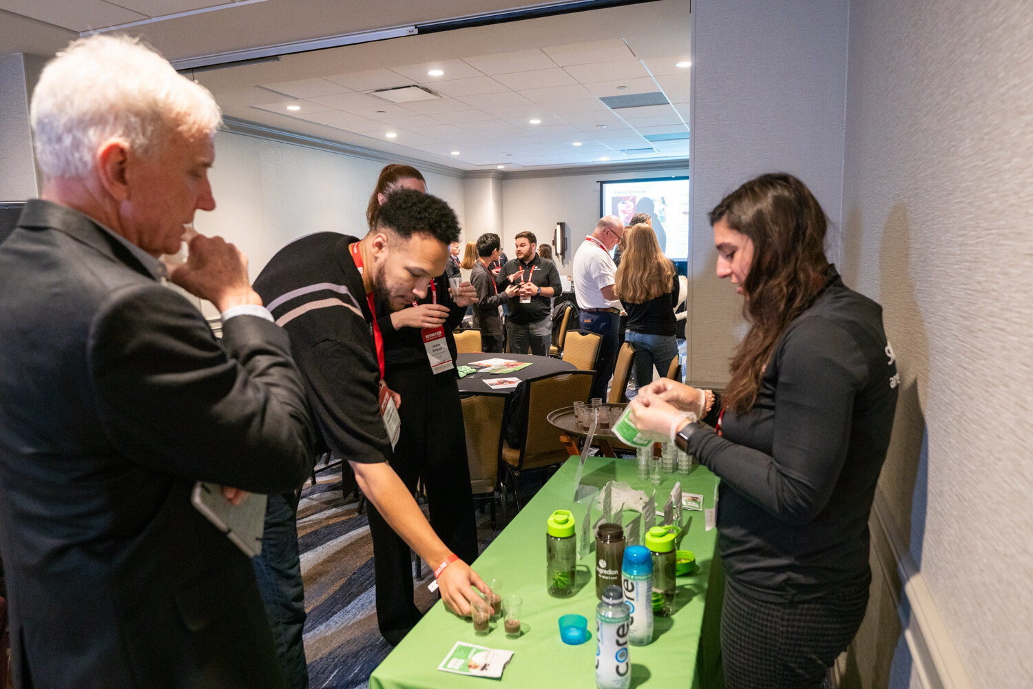 Several attendees sample drinks at a green Ingredion table.