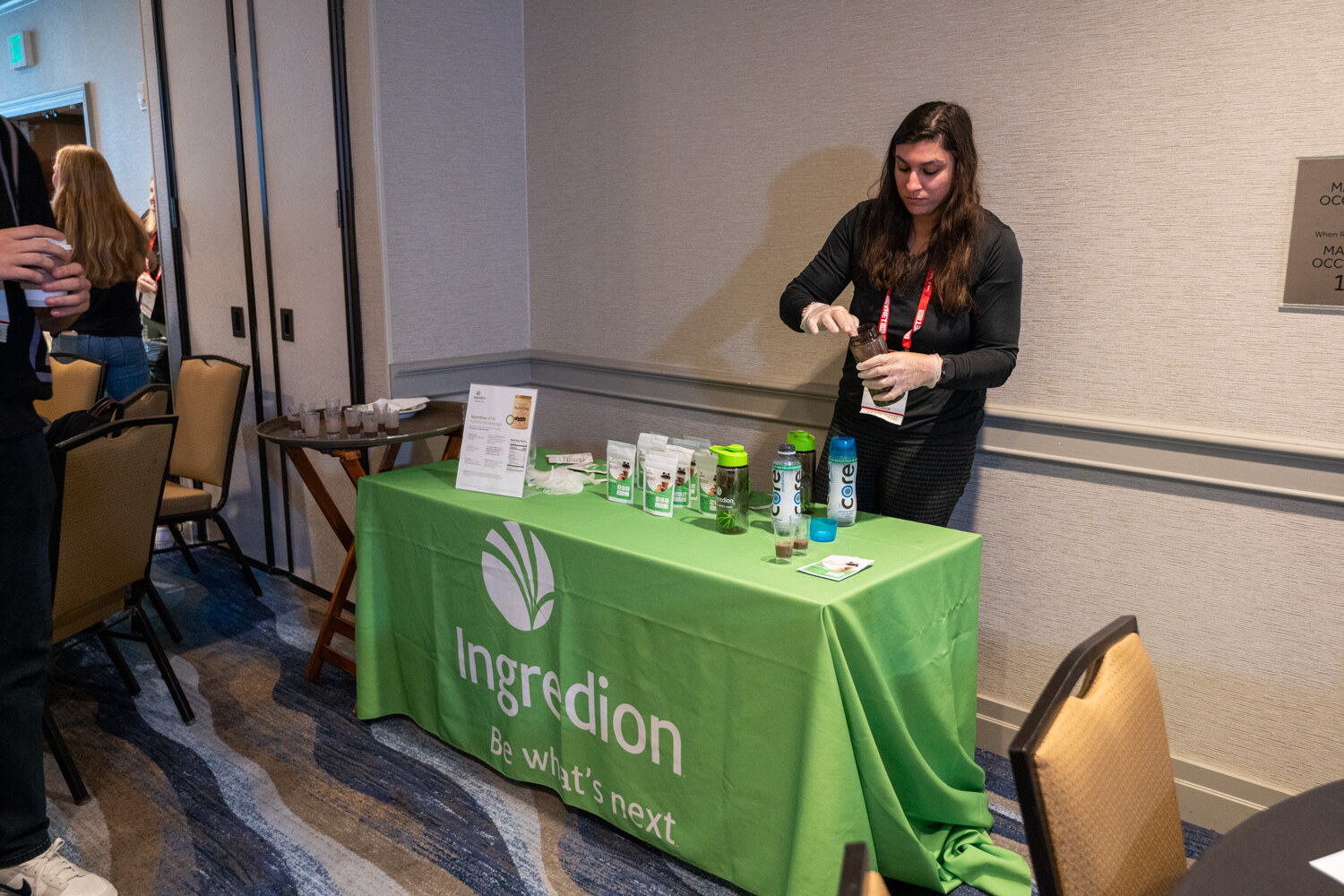 A woman in black pours samples at a green Ingredion table.