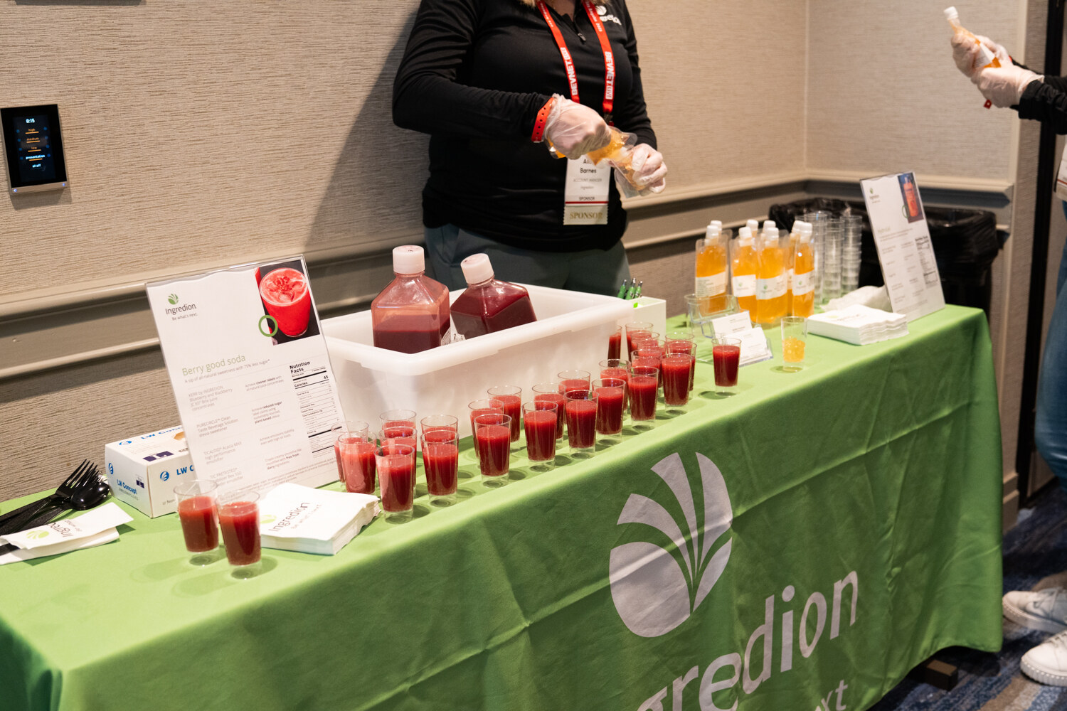 A table covered in a green Ingredion cloth holds rows of red sample cups.