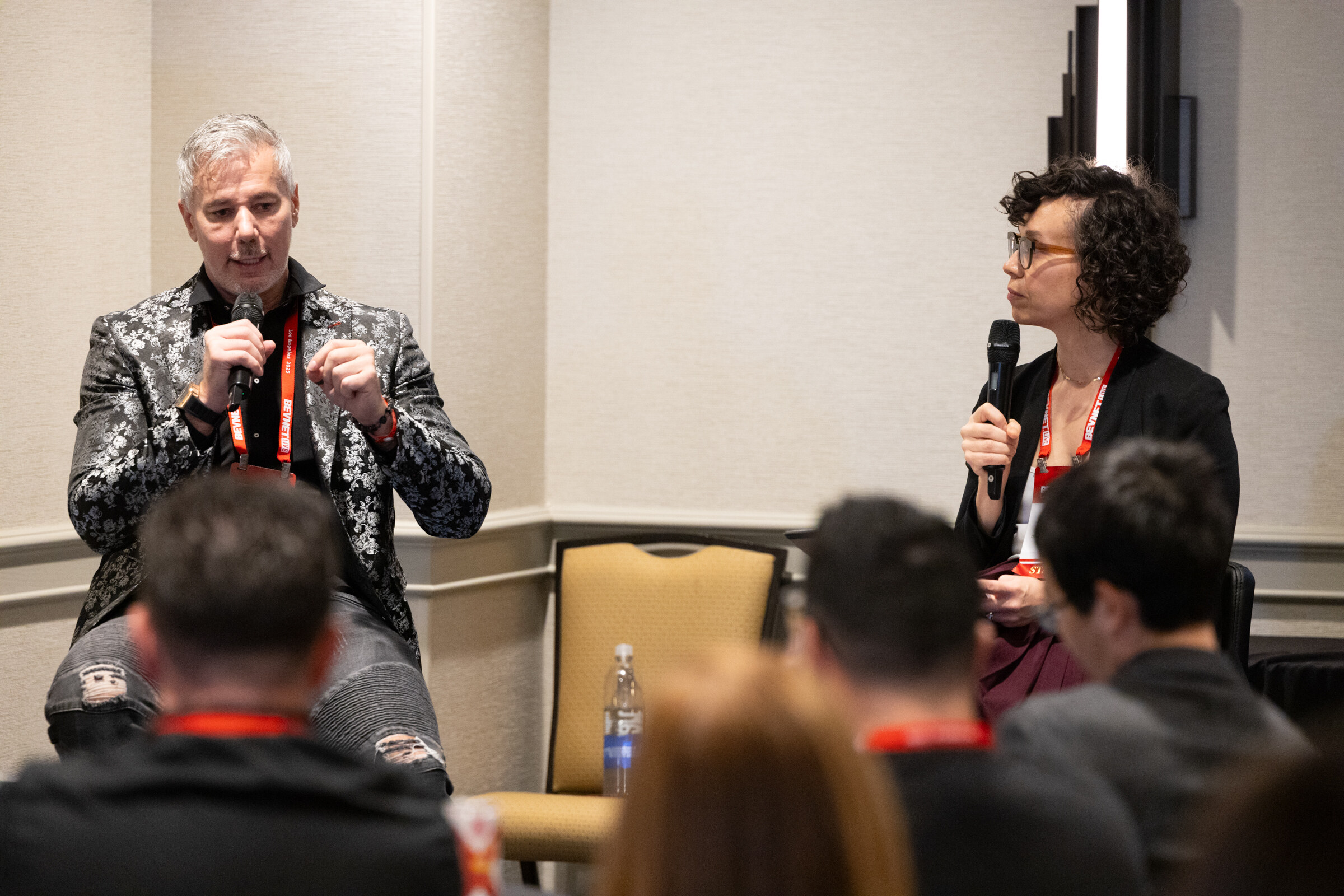 A man in a patterned jacket and a woman moderator speak into microphones.