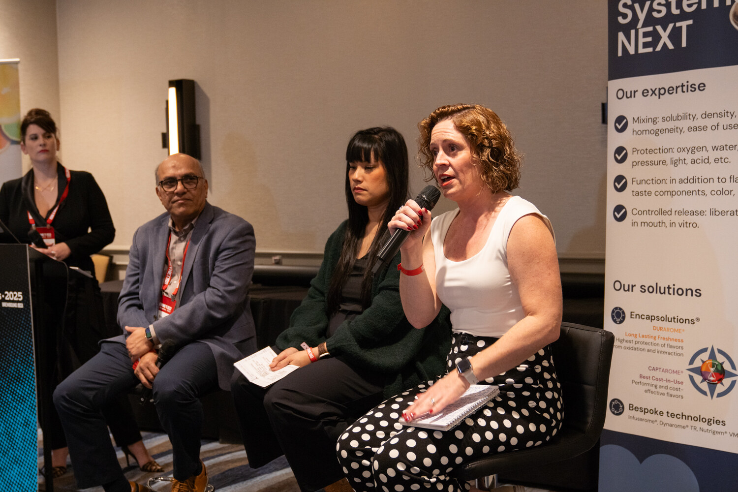 Four panelists sit in front of a SystemNEXT banner.