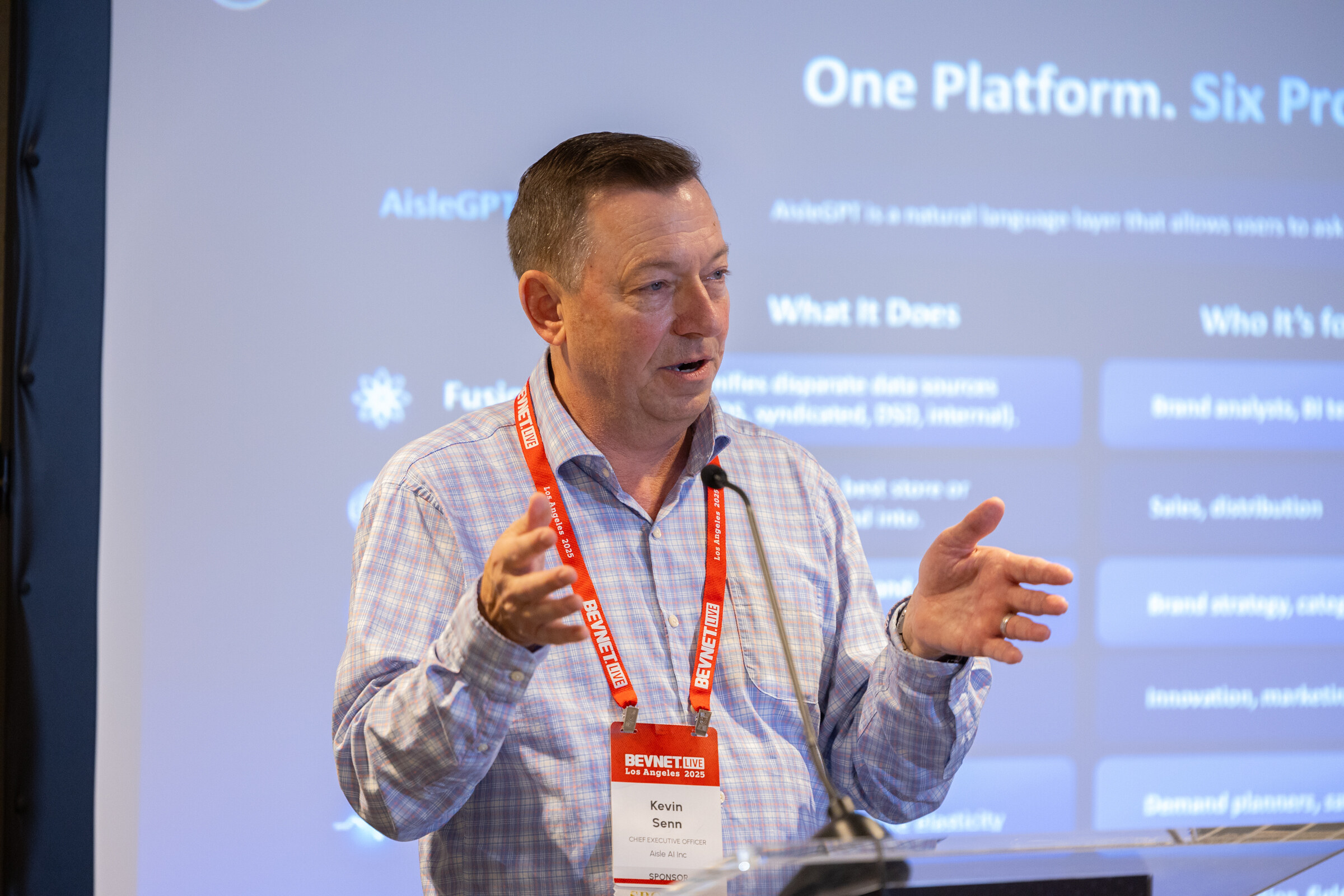 A man in a checked shirt speaks in front of an AisleGPT slide.