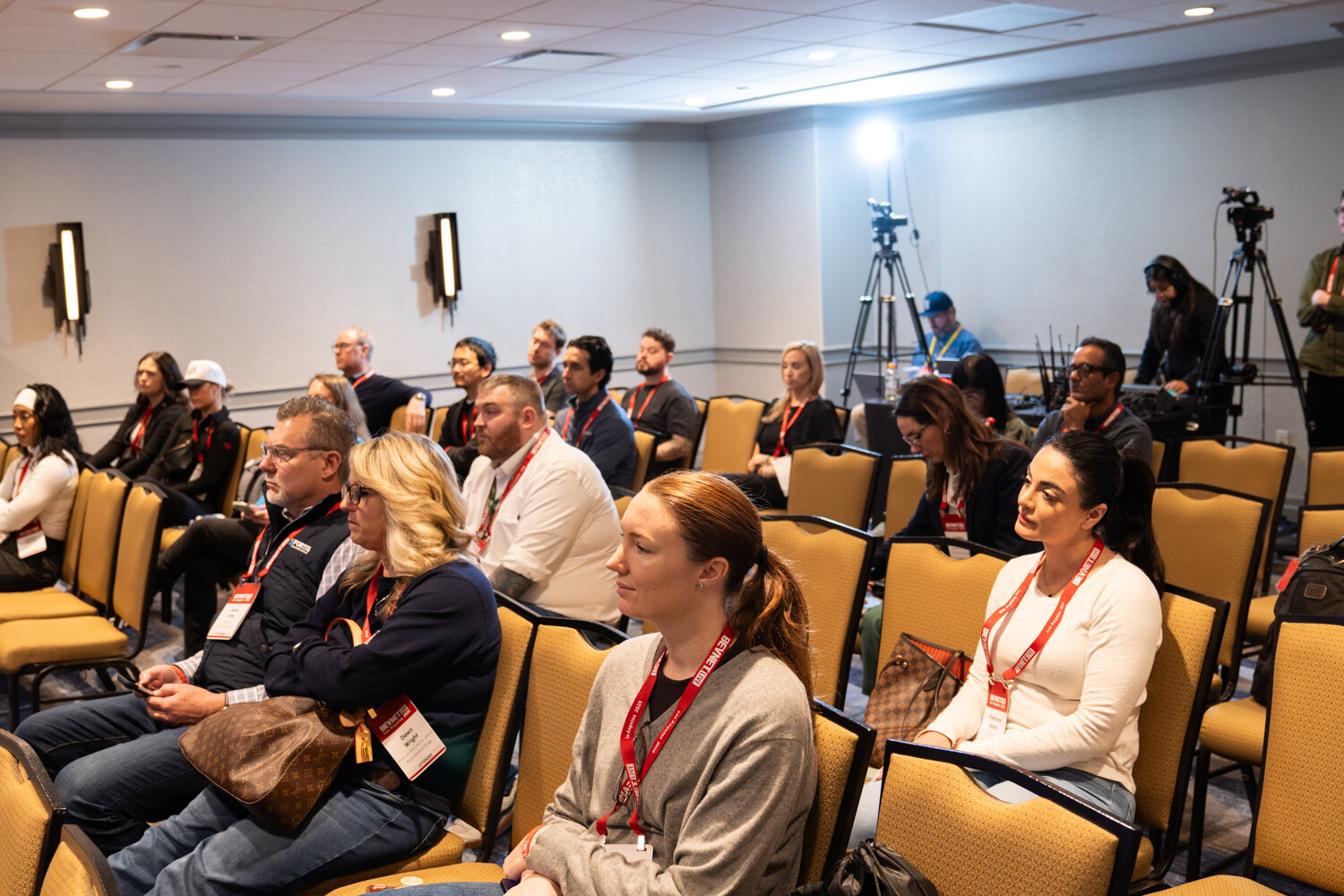 Attendees sit in rows of chairs in a meeting room.