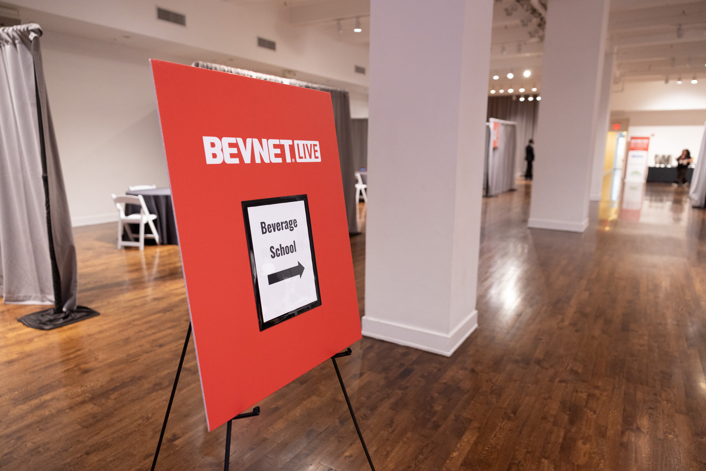 Red BevNET Live easel sign with an arrow reading “Beverage School” in an empty hallway.