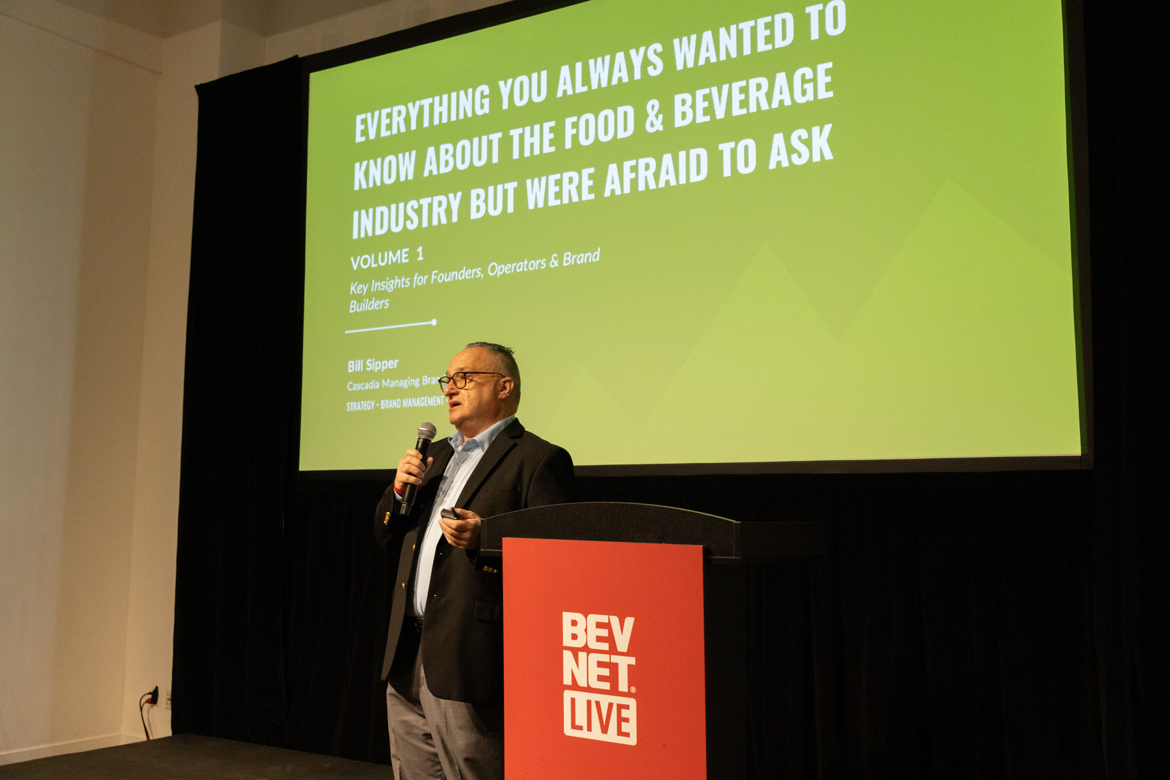 Speaker at a red BevNET Live podium beside a green title slide for the session.