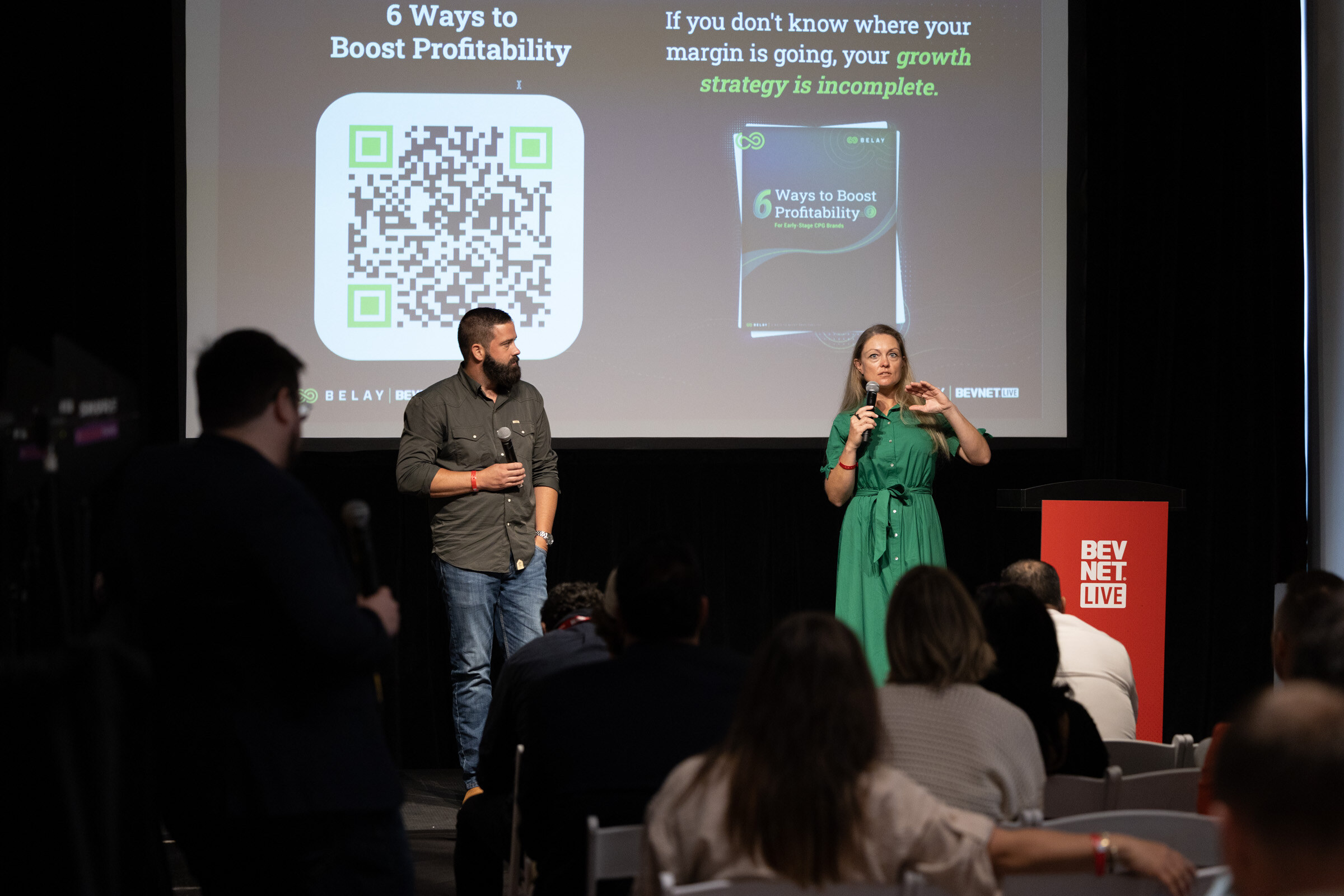 Two presenters on stage before a slide with a QR code titled “6 Ways to Boost Profitability.”