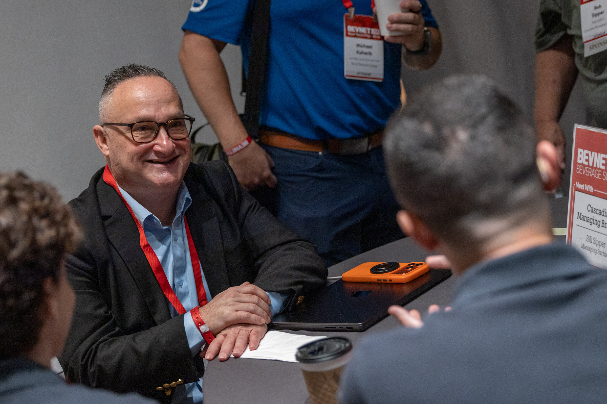 Smiling man in glasses at a table with a Cascadia Managing Brands “Meet With” card, talking with attendees.