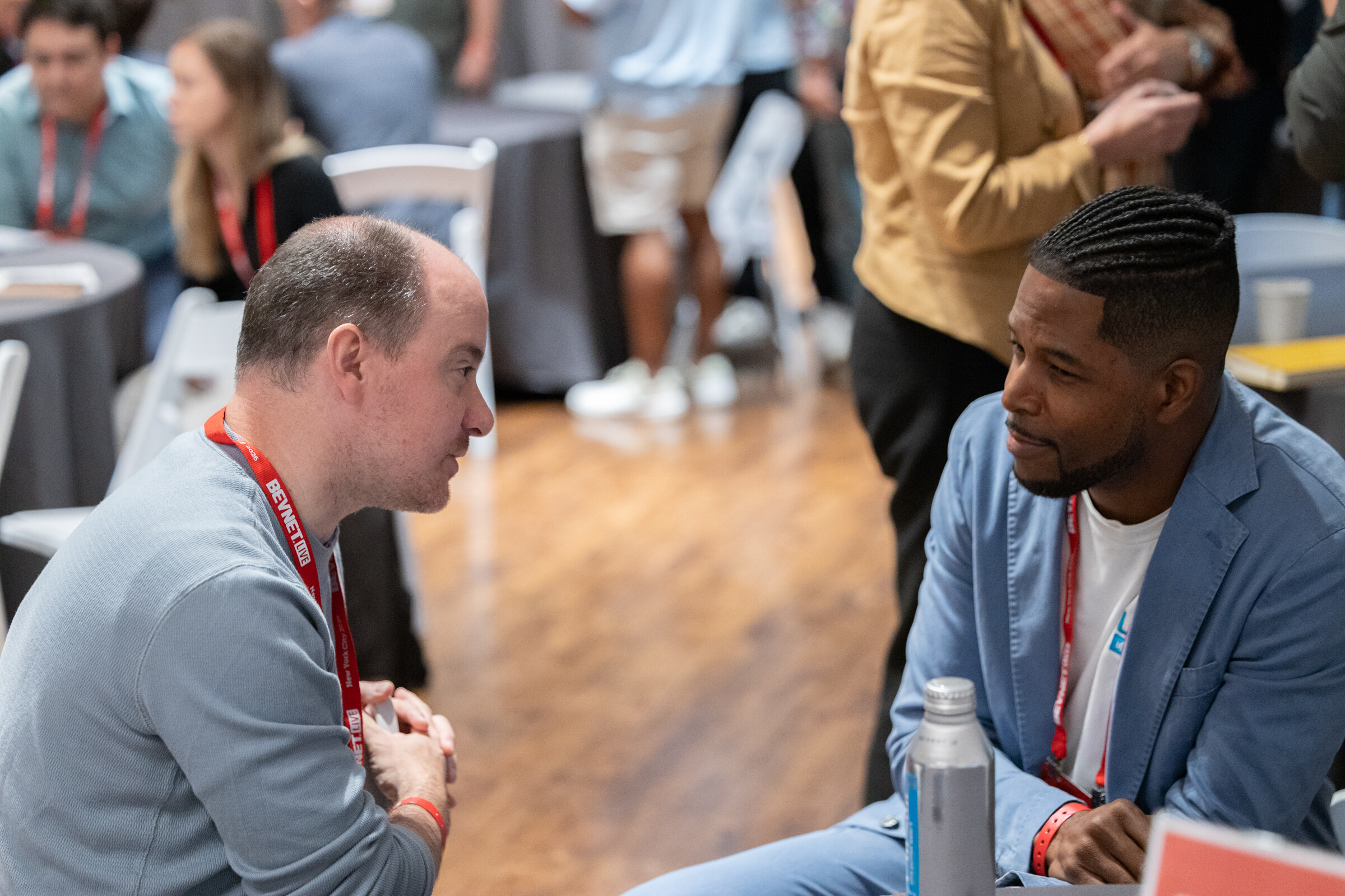 Two men leaning in toward each other in conversation at a roundtable.